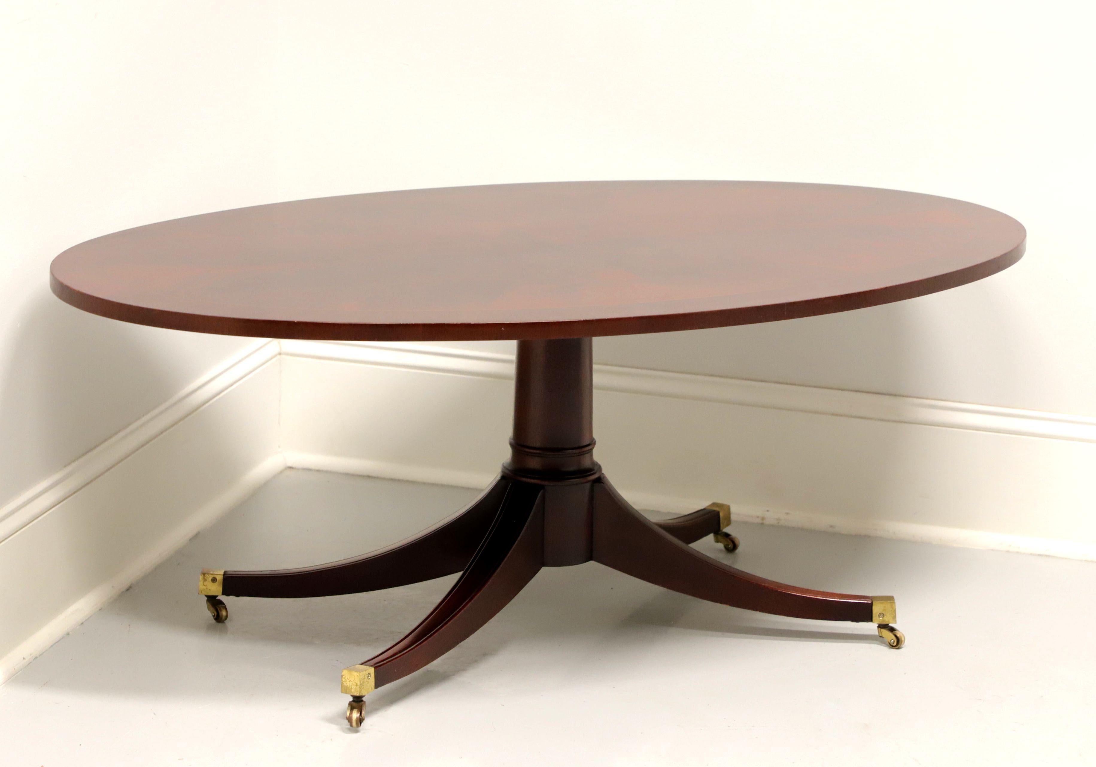A vintage Georgian style oval coffee table, unbranded, similar quality to Councill or Hickory Chair. Solid mahogany with banded flame mahogany top, round single pedestal base with four curved legs and brass toe caps with brass casters. Made in the