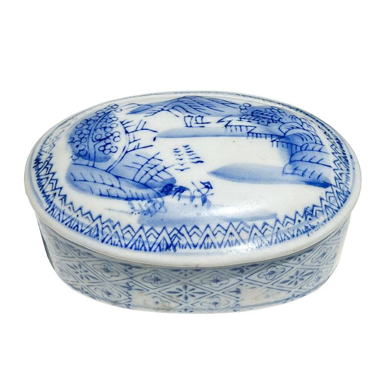 Un petit plat à bibelots ovale de chinoiserie bleu et blanc avec un couvercle. Cette pièce provient de Chine et a été réalisée en céramique avec de la peinture bleue. Il est blanc, avec un motif scénique peint sur le dessus, et un motif géométrique