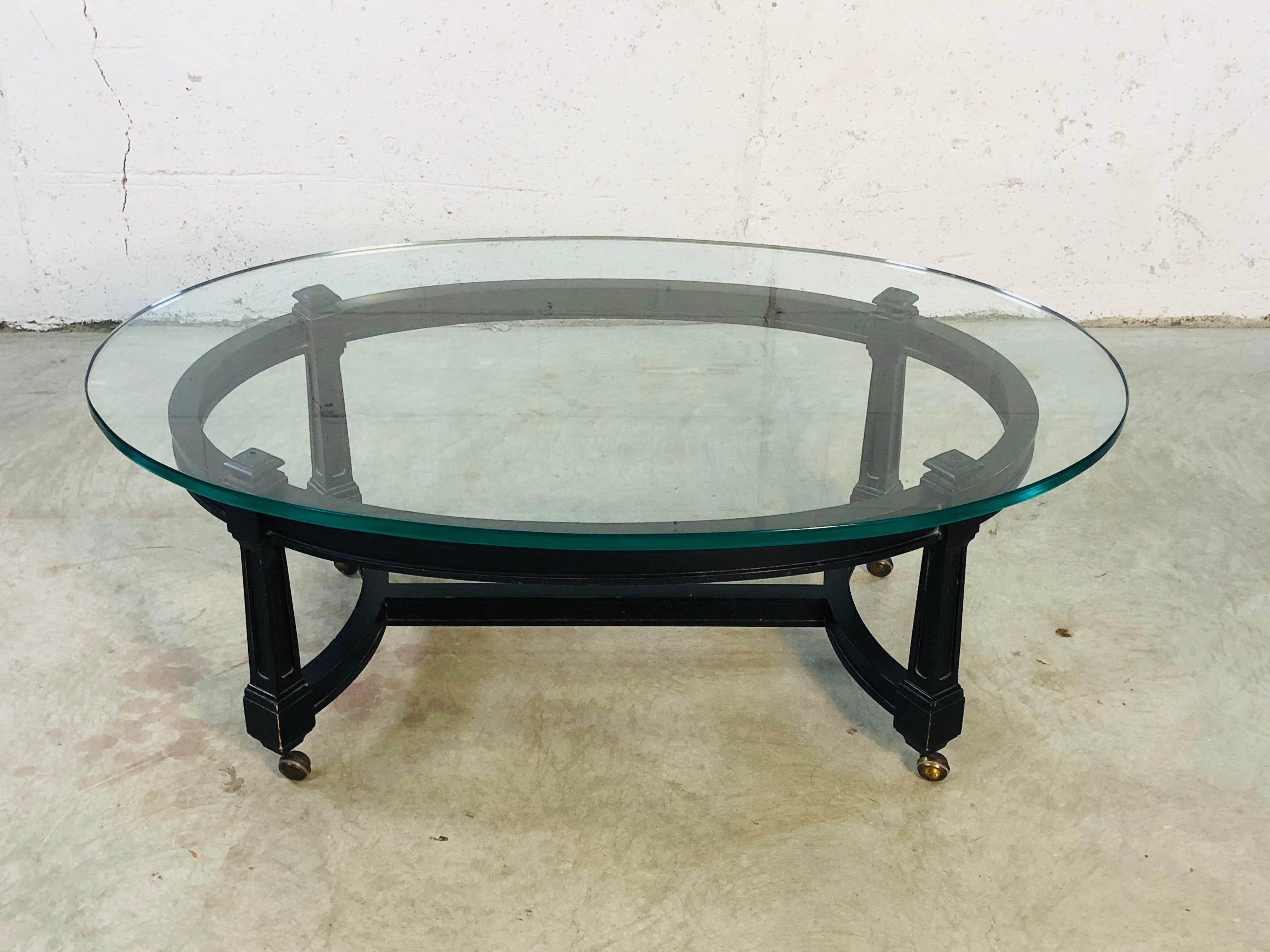 Vintage 1970s oval glass top coffee table with a black wood base. The base is on casters and the table moves freely. The glass is .75” thick and very heavy. There are no marks but it looks like Century Furniture. The base only measures 39” L x