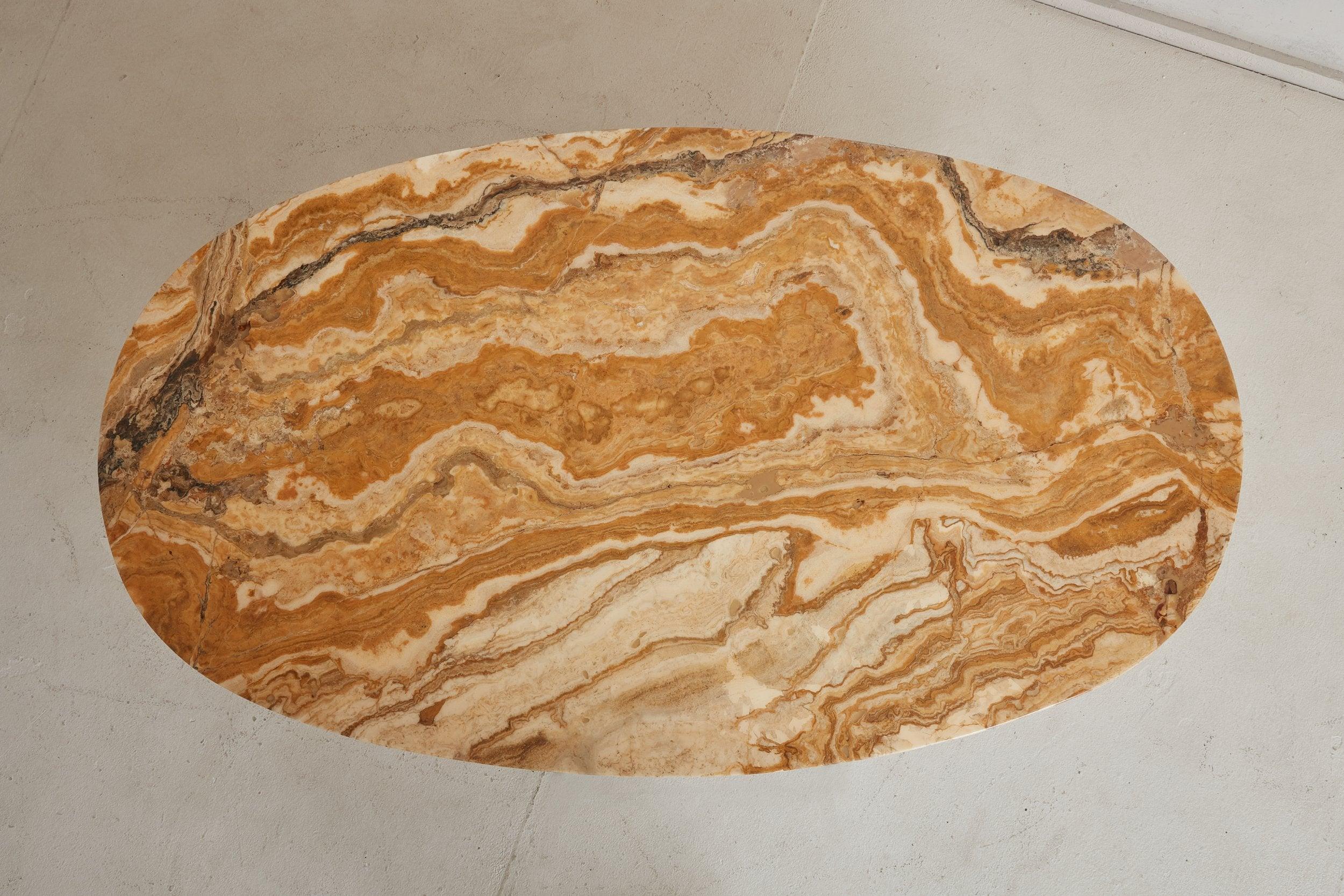 A vintage coffee table featuring a smooth, oval onyx top with stunning veining in a range of warm ochre, cream, and ebony hues. The 2” thick top elegantly rests on a patinated chrome pedestal base composed of fluted “X” form legs and narrow,