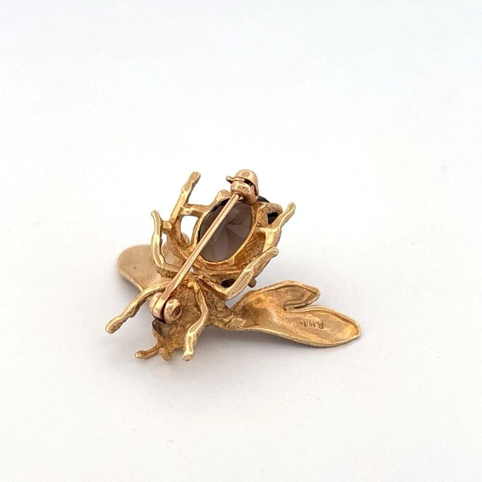 This vintage 14K yellow gold bee brooch is a beautifully crafted statement piece, featuring an oval faceted smoky quartz gemstone measuring approximately 12 x 10.13 x 6.79mm, with an estimated weight of 4 carats. The brooch is designed with
