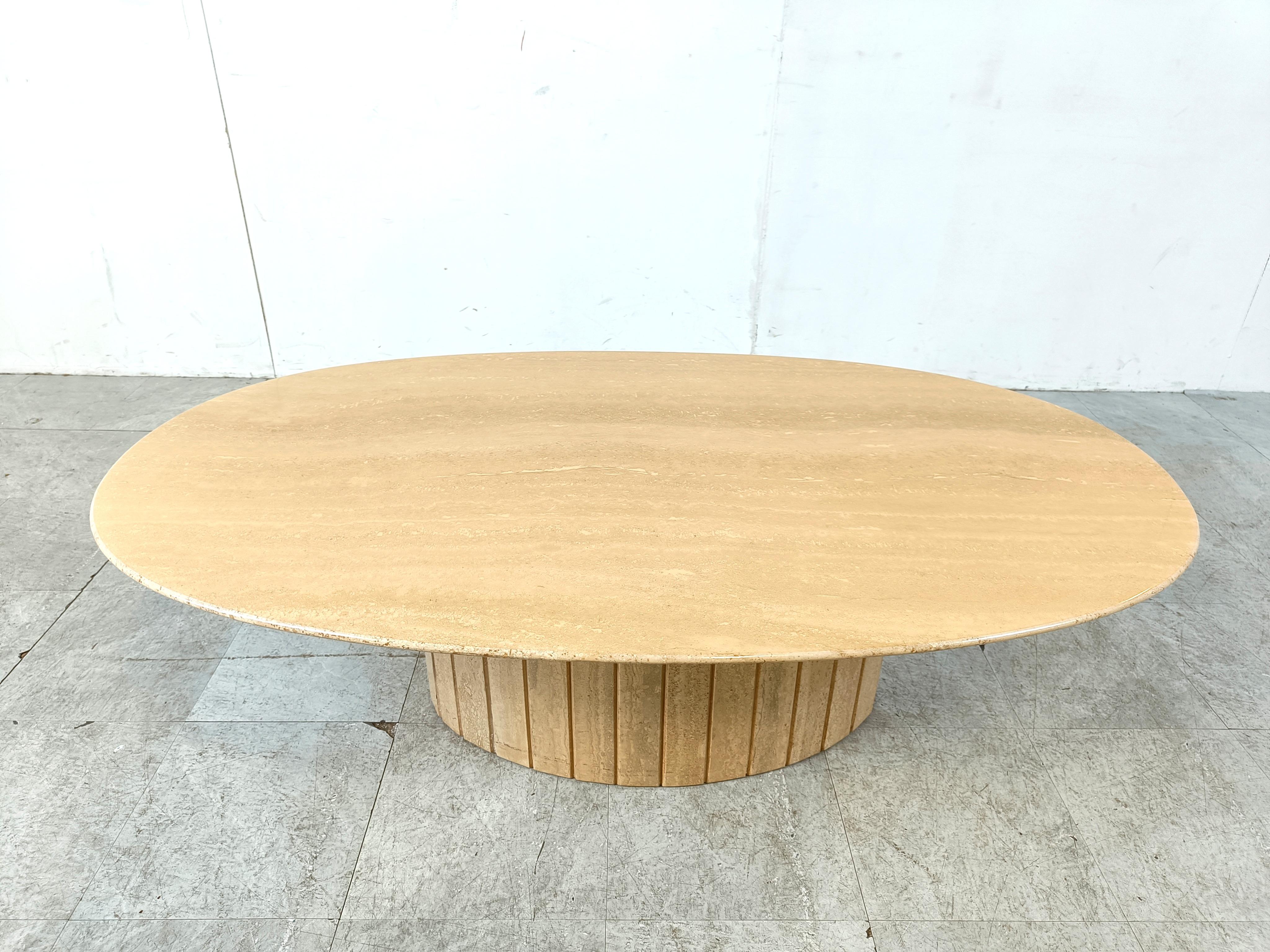 Eleganter Couchtisch aus Travertin mit einer ovalen, messerscharfen Tischplatte, die auf einem Sockel aus geriffeltem Travertin ruht.

Dieses zeitlose Stück bringt einen Hauch von Charme in Ihr Wohnzimmer.

Sehr guter Zustand.

1970er Jahre -