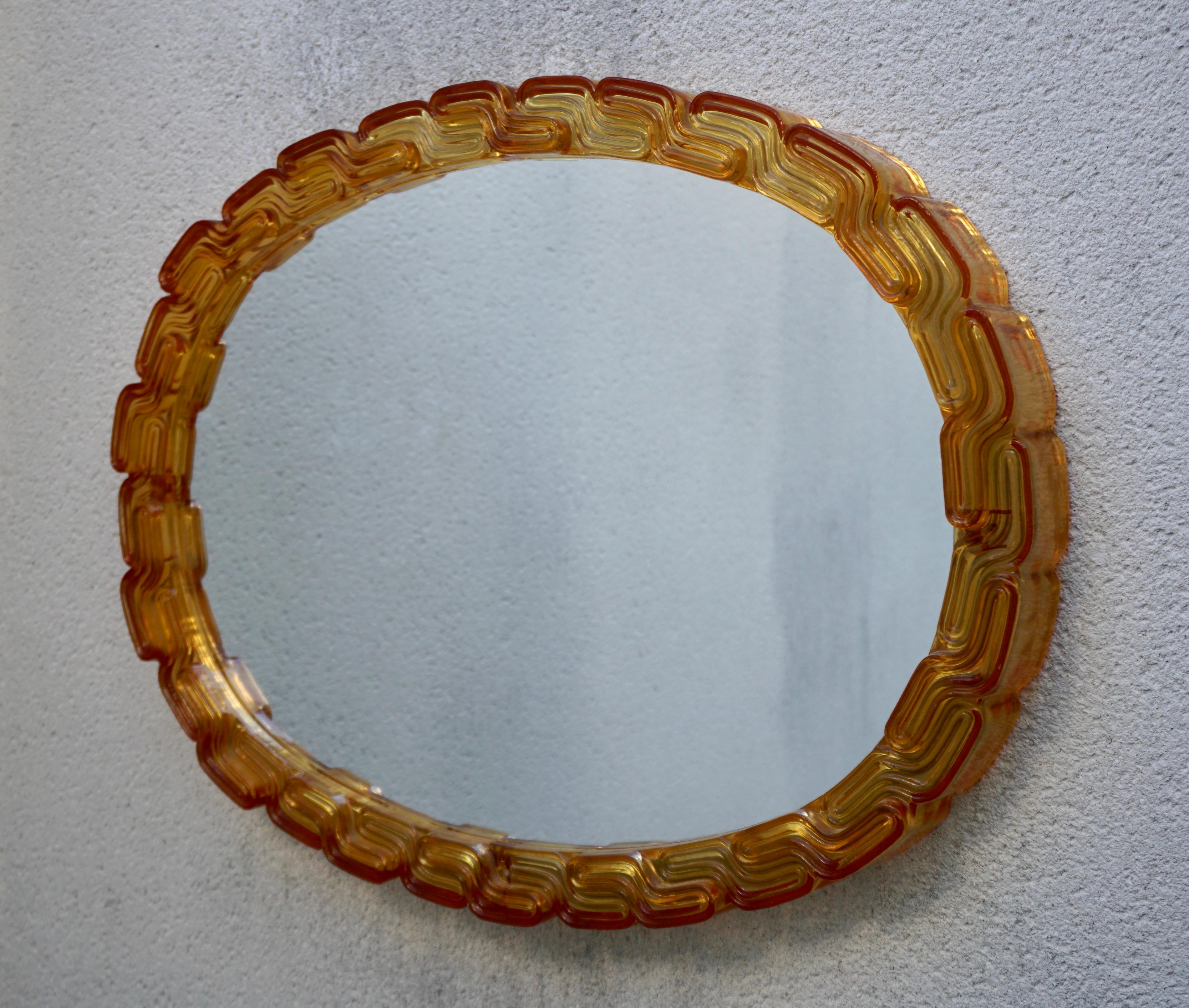 An oval acrylic wall mirror made in the 1970s in Italy. The mirror has an oval acrylic design in an amber orange color.

Width 26.7