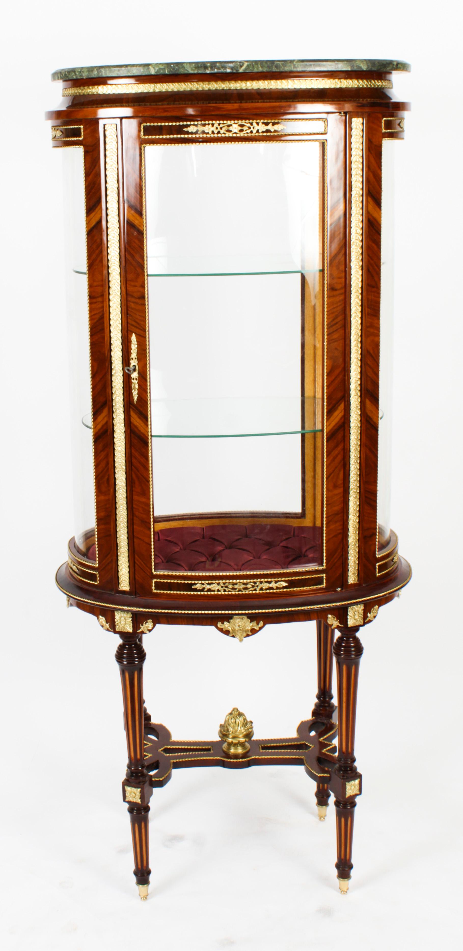 This is an exquisite walnut and ormolu mounted oval display cabinet surmounted with a Verde Antico marble top. This elegant display cabinet will soon become the centrepiece of your furniture collection and can suitably house your most valued