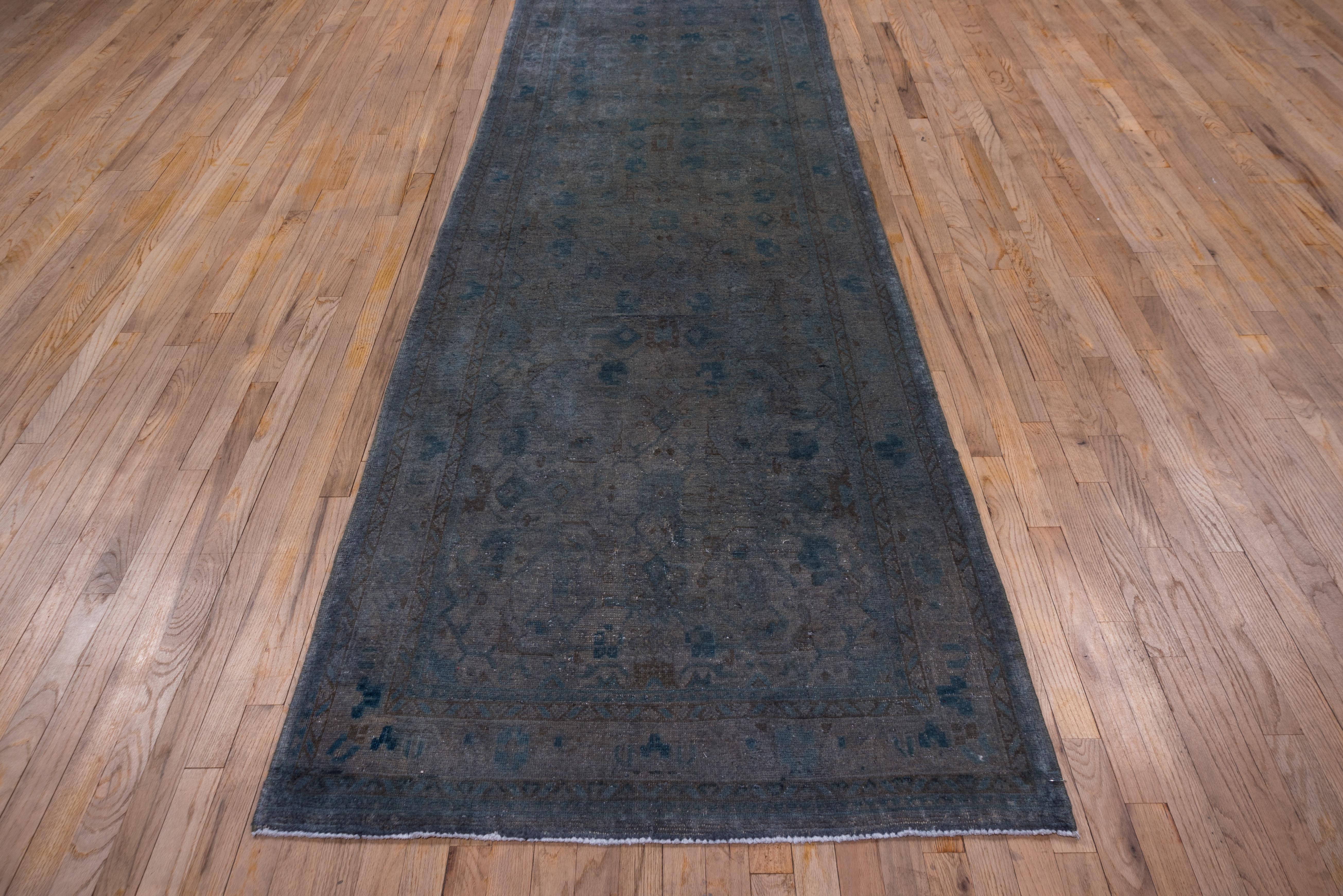 Overdye rugs are generally vintage with a recent monochrome overdye which obscures the original design. In this example, the overdye is a grey-green. Only the minor borders show at all through the overdye. The original palmette pattern is only a