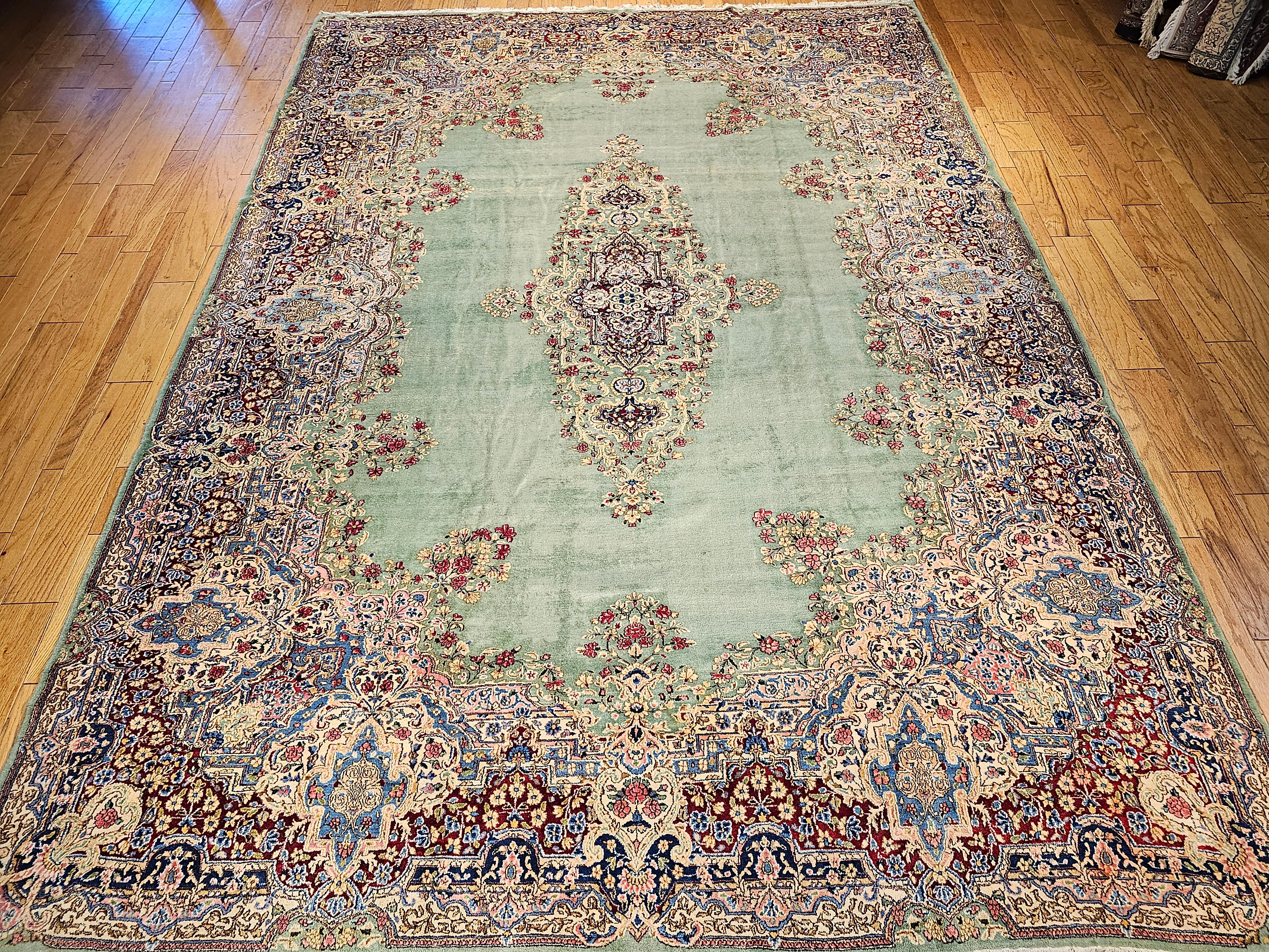 The oversized vintage Persian Kerman carpet has a very soft and unique and highly desirable pale green background color circa the 1940s. The Kerman rug has a wide border with a floral design and bouquets in brilliant colors of red, green, pink, and