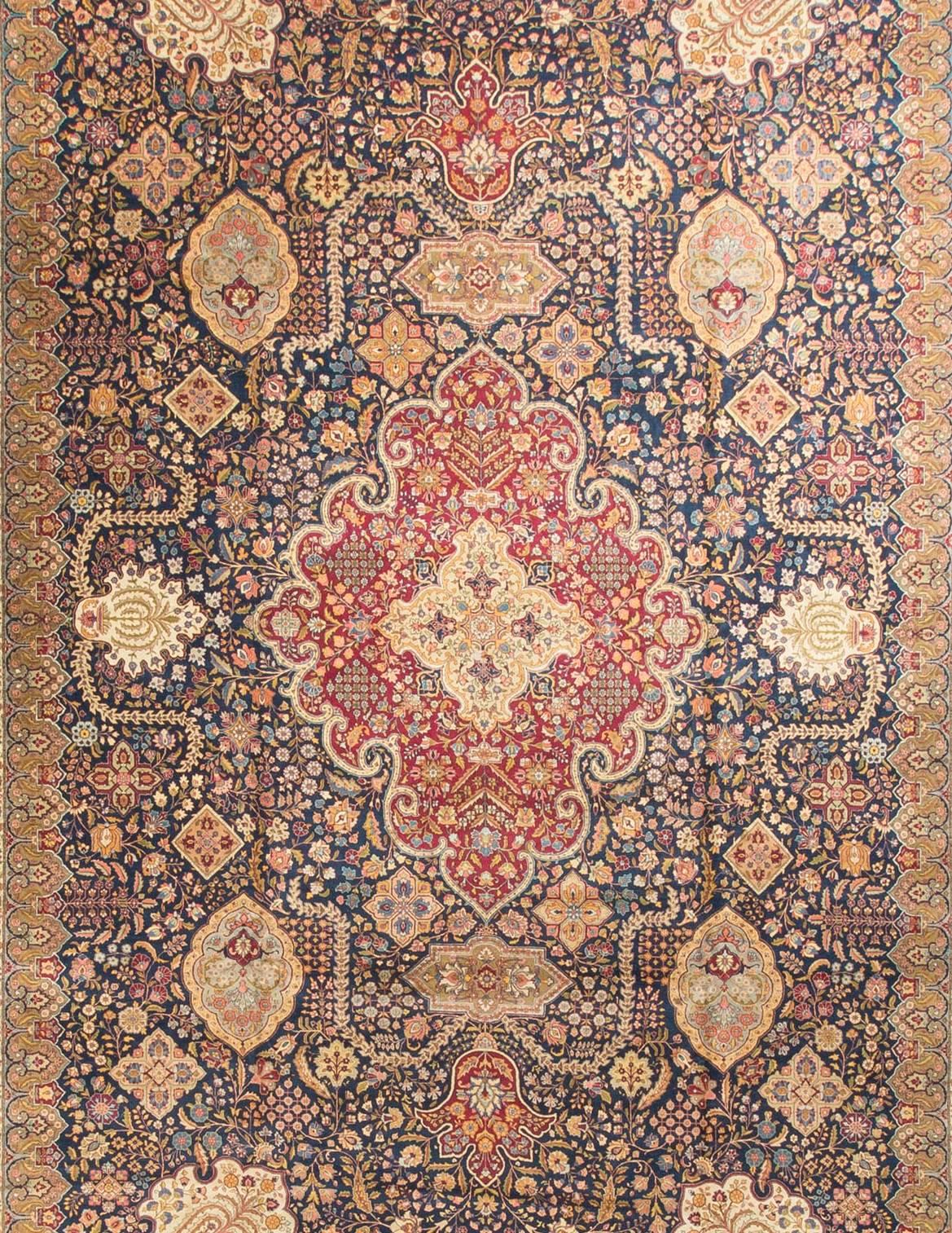 A central medallion surrounded by a field filled to overflowing with floral elements on a dark blue ground the details of which show the skill of both the designer and master weaver. The main border in red surrounded by two guard borders in ivory