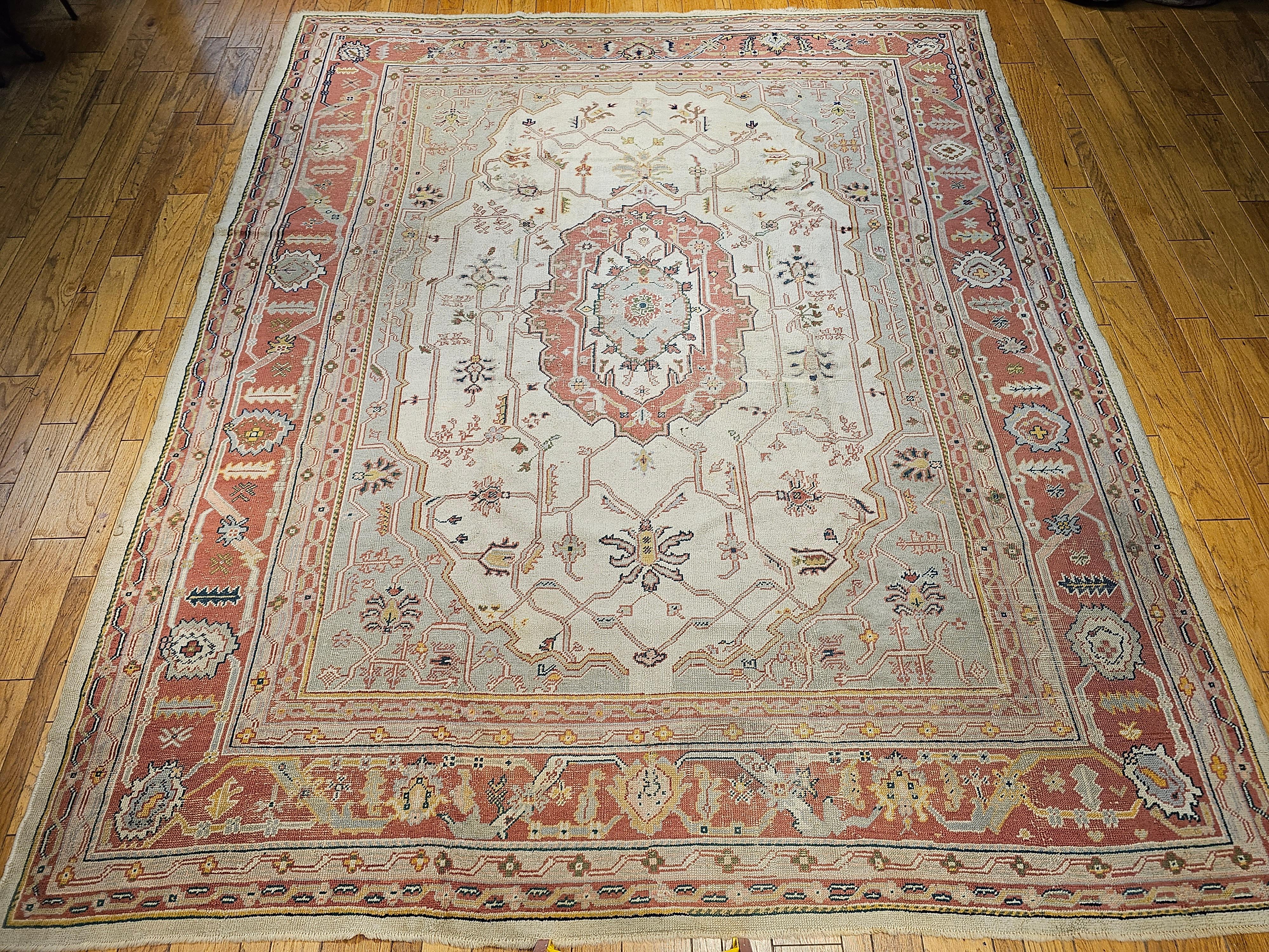 A “near square” oversized Turkish Oushak in a geometric medallion pattern from the early 1900s in soft shades of pink, green, yellow, and ivory.  It is in the style of the Persian Serapi rugs from the mid-1800s.  It has an open design set in a cream