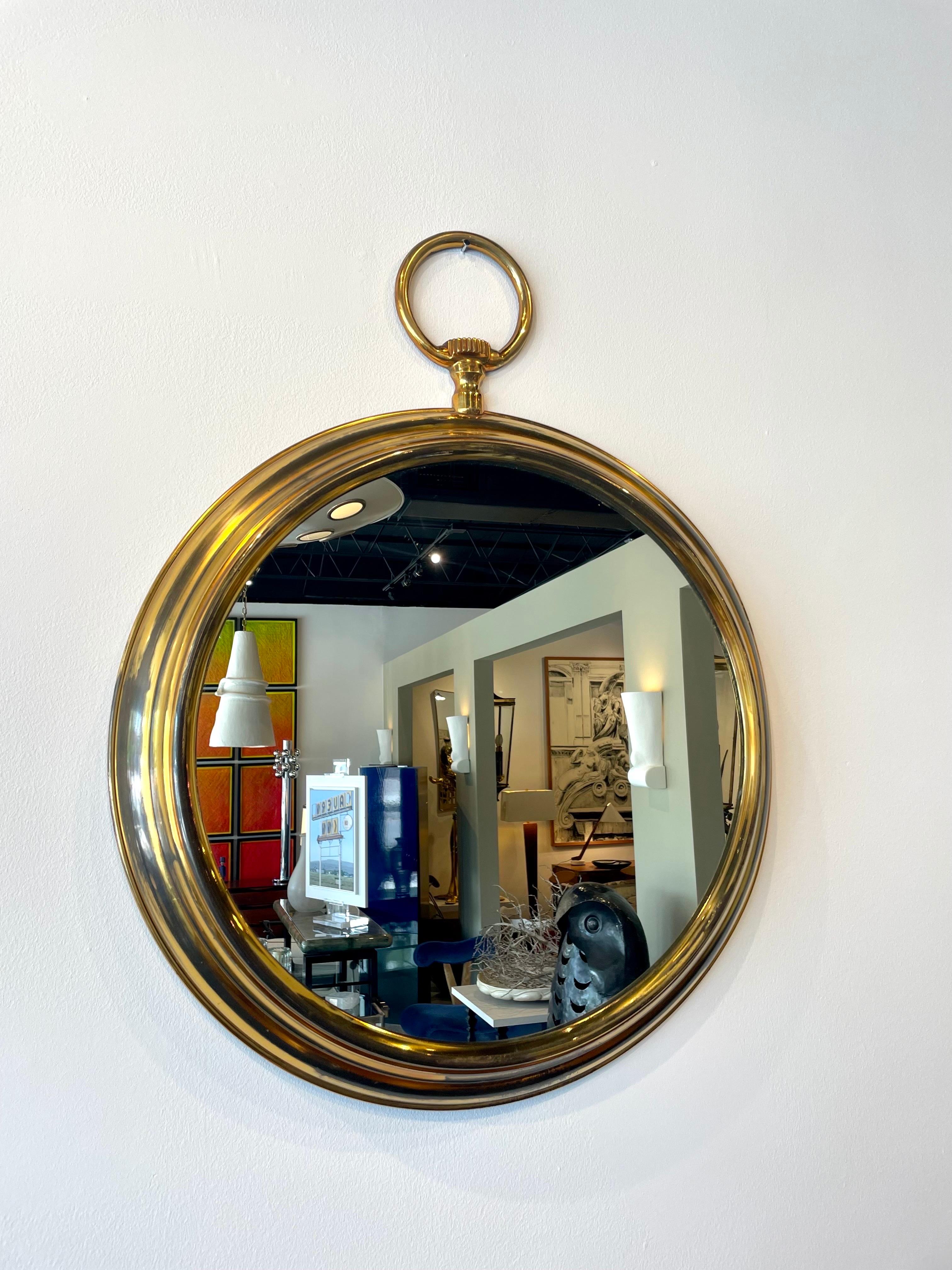 This very large (largest of its kind) eye-catching brass pocket watch shaped wall mirror in the style of Piero Fornasetti. Beautiful details from the winding mechanics to the waves of brass on frame. This wall mirror will be a nice midcentury