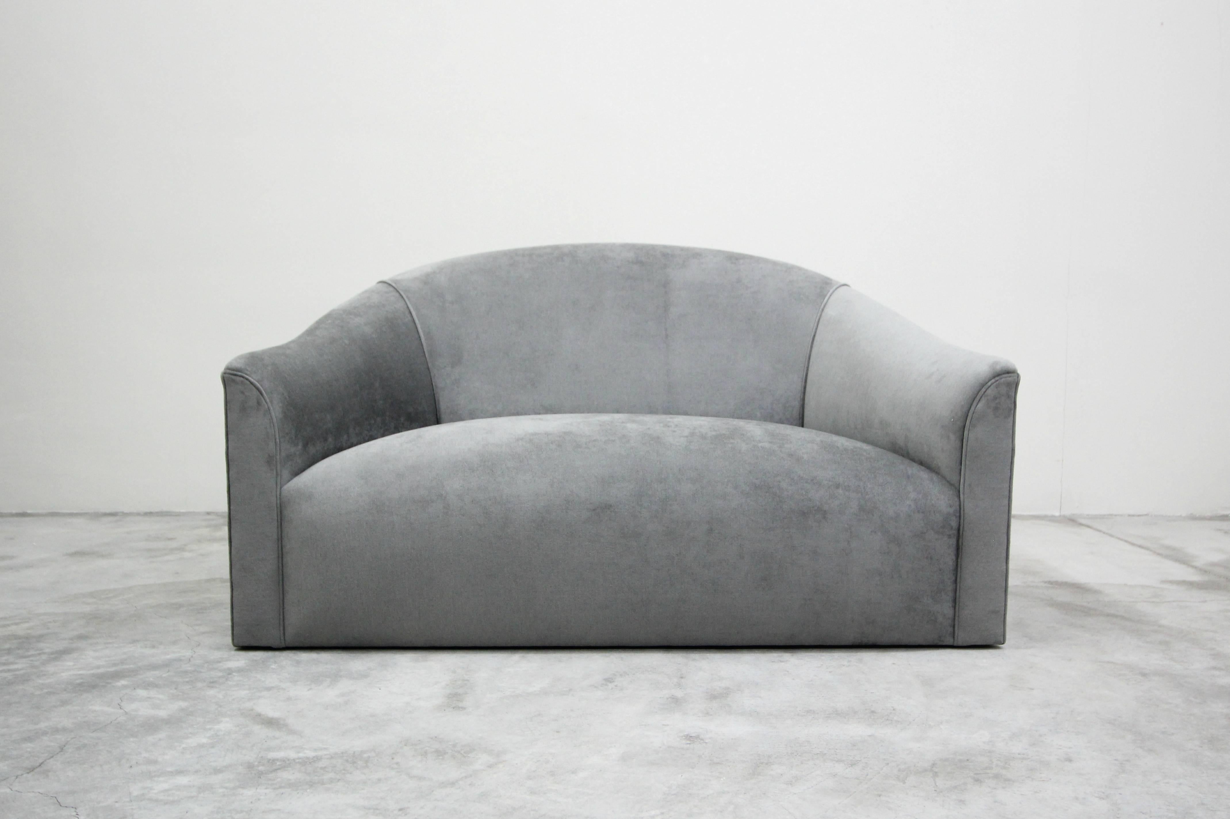 Previously this incredible piece was covered in a soft white leather that had seen better days. We brought its incredible lines back to life with all new gray velvet. This piece can be used as a loveseat or an oversized chair, it seats two