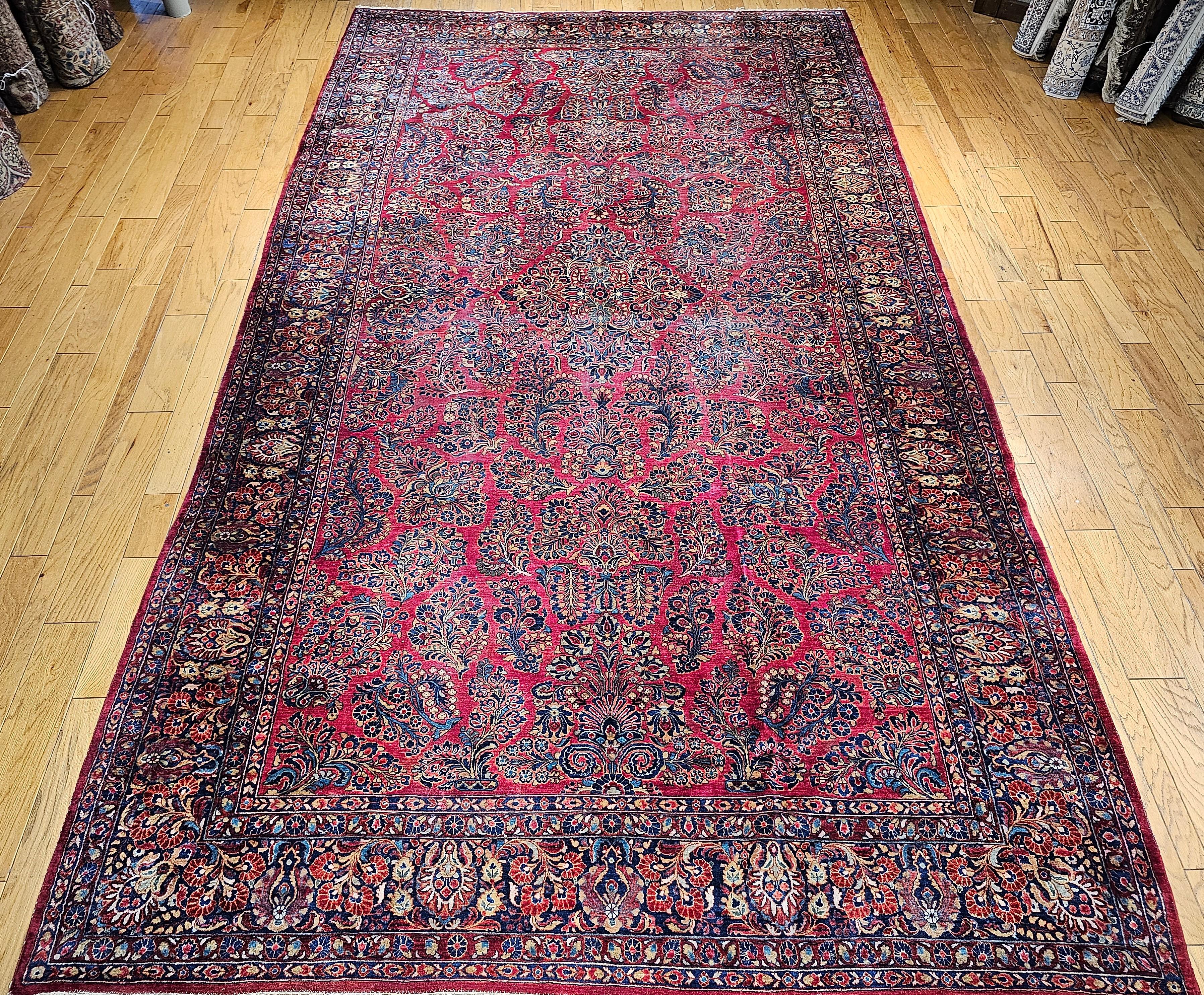 Vintage Oversized Persian  “Painted Sarouk”  in an all-over pattern consisting of large flower bouquets set on a bright red background with a navy blue border also filled with flower bouquets.  The color of bright red which is often referred to as