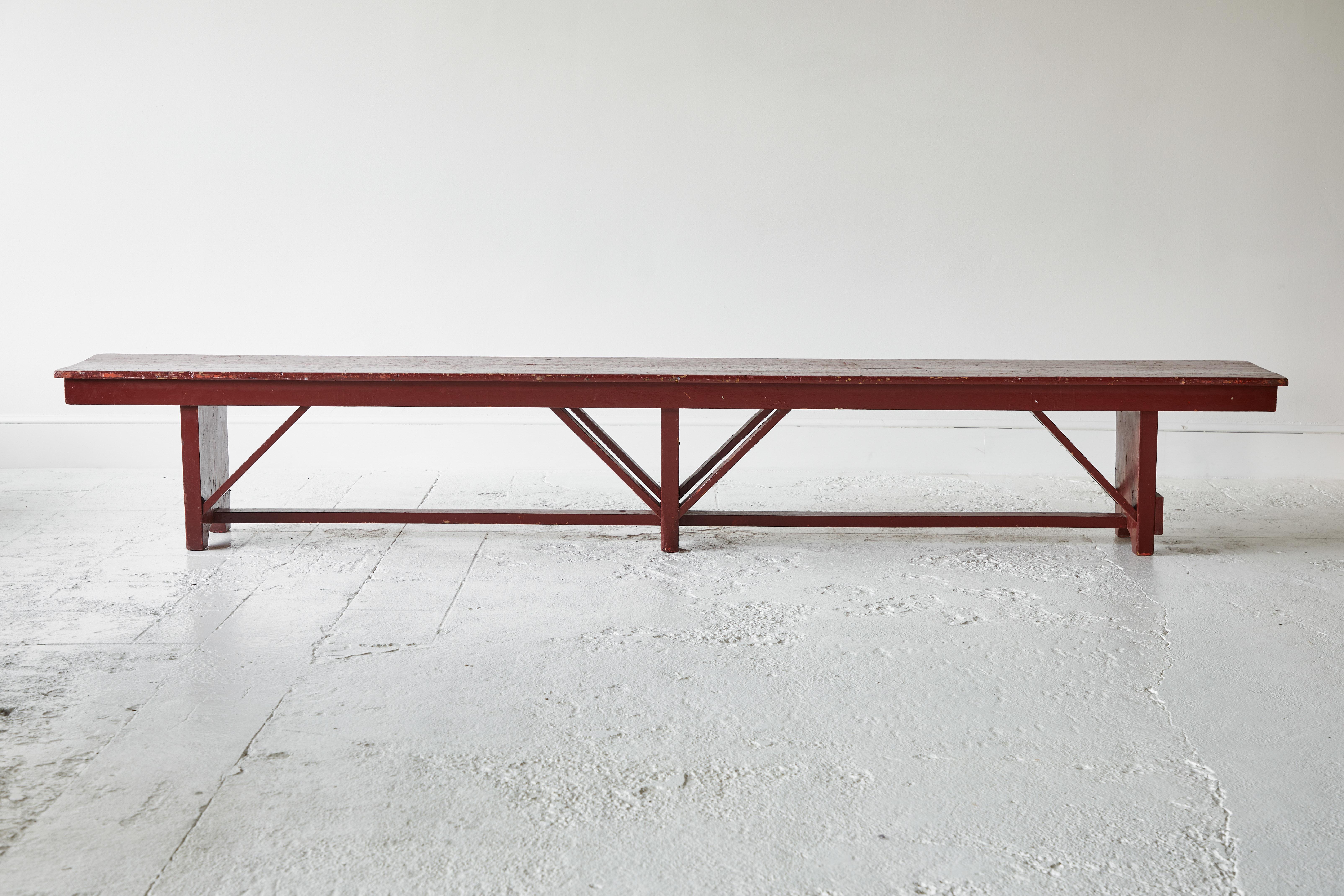 Vintage wooden bench painted oxblood red with cross bars and a center leg support. The paint has not been altered which adds to the character and charm.
 