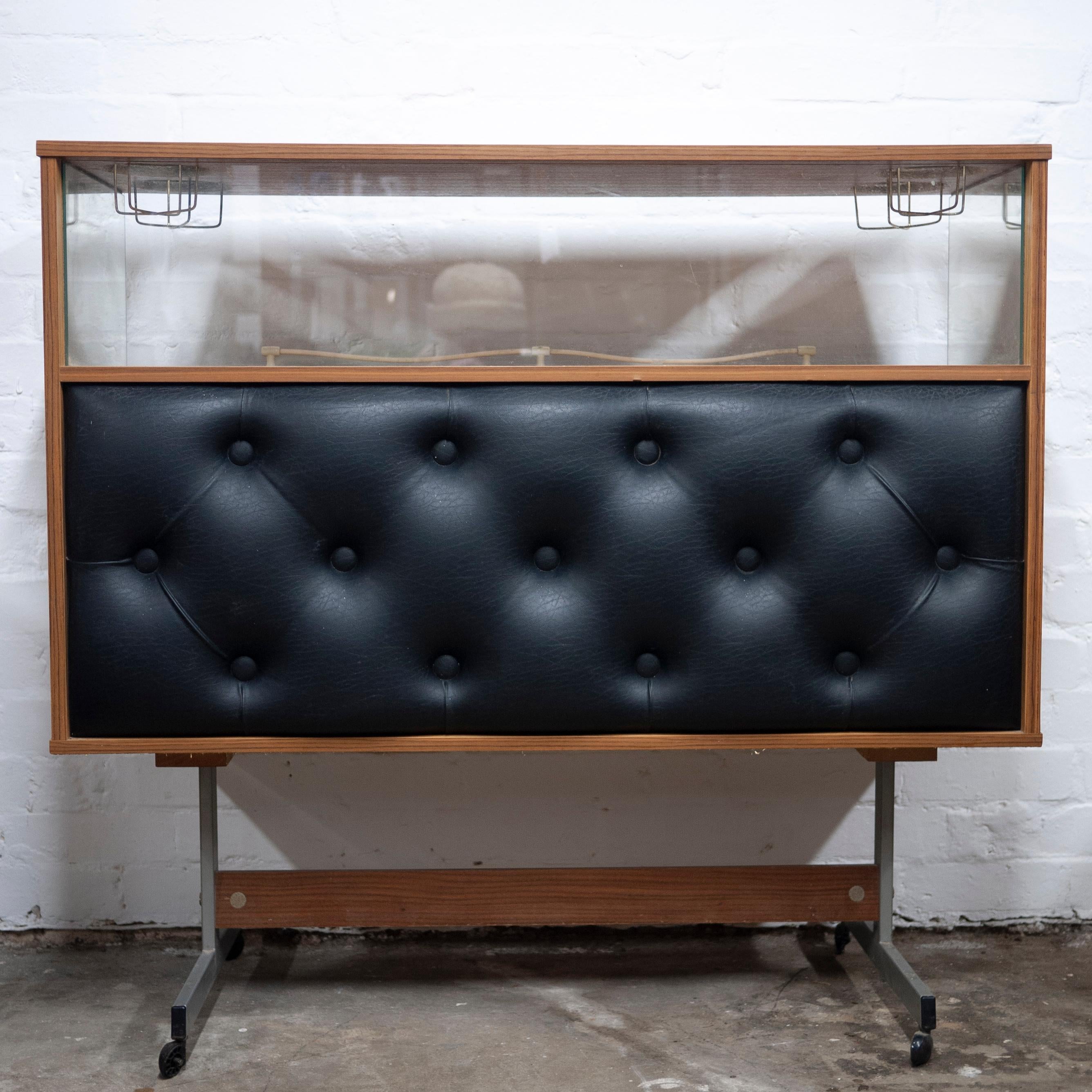 A vintage 1960s home bar with a black vinyl studded front. The bar features 4 top drink holders.

Manufacturer -n/a

Design Period - 1960 to 1969

Country of Manufacture - Unknown

Style - Vintage

Detailed Condition - Good with minimal