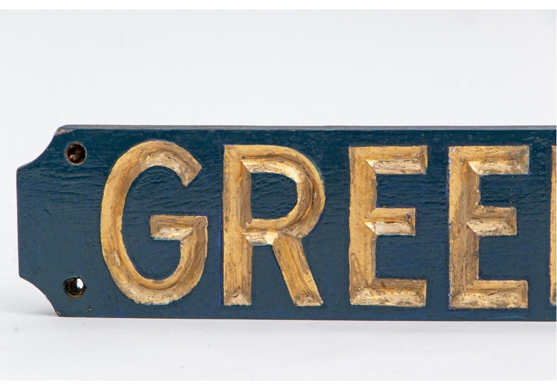 A solid mahogany board with a gentle curve having deeply carved and gilt letters spelling the town name, “GREENWICH”. Deep Blue background paint. With a cord on the back for hanging and four holes for screws at each corner. Very good condition with