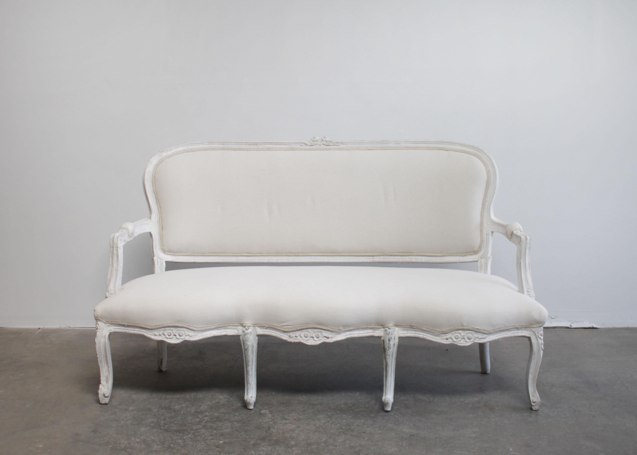 Vintage painted and upholstered Louis XV style open arm sofa settee
Painted in a French white with subtle distressed edges.
Classic cabriole legs, with a floral carvings, and double flower carvings at the top back of the settee.
Upholstered in a