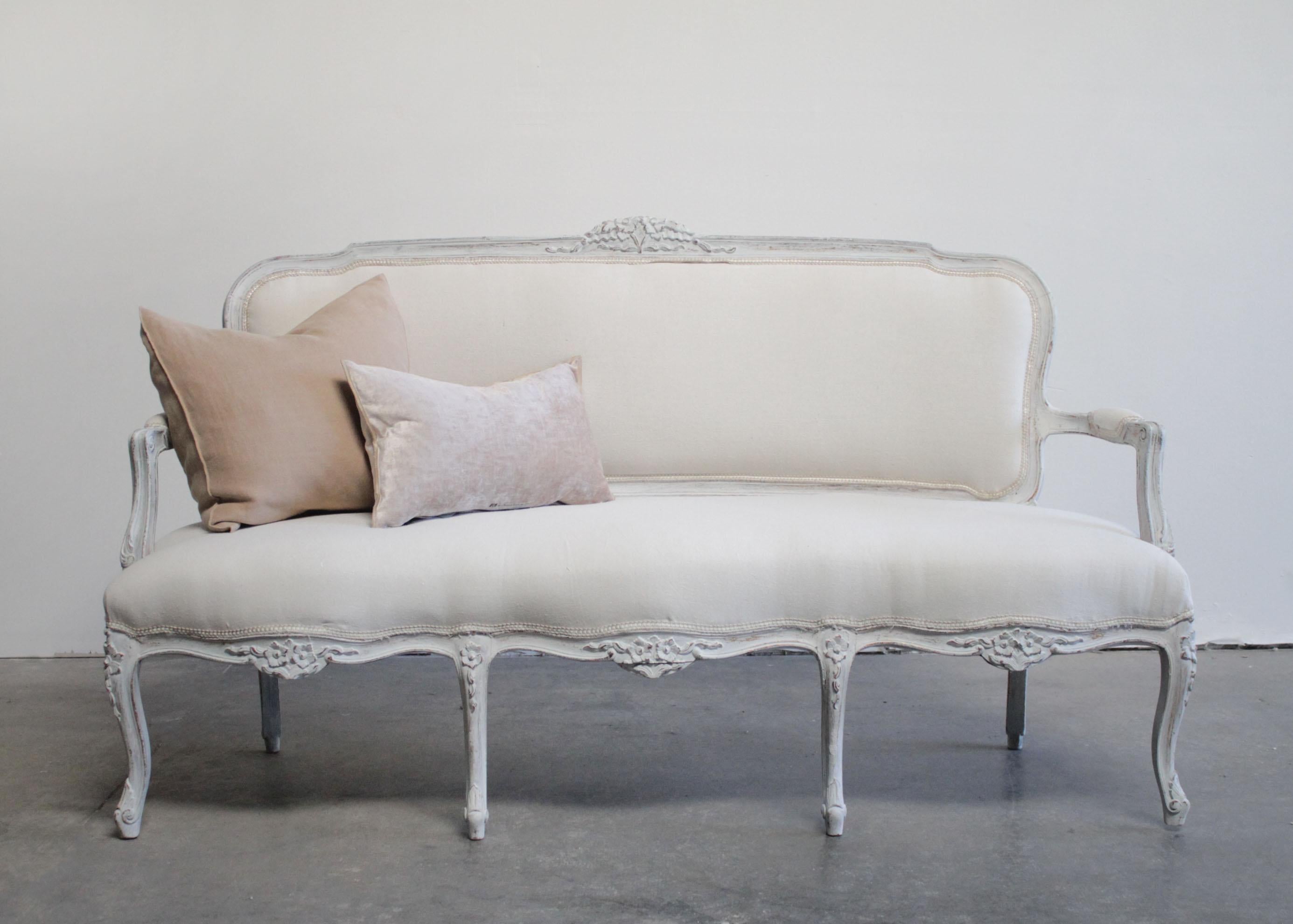 Vintage painted and upholstered Louis XV style open arm sofa settee
Painted in a French gray with subtle distressed edges, where gilt and wood show through.
Classic Louis XV legs, with a medallion carving, and large rose and flower garland