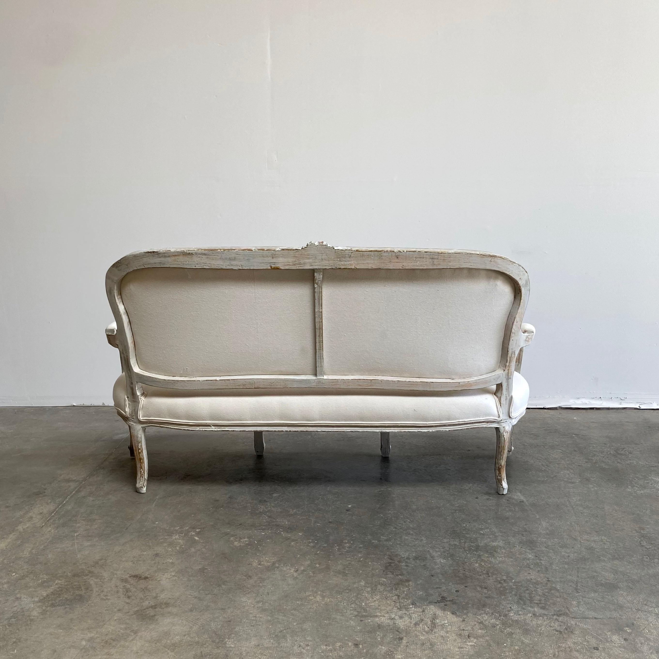 Vintage painted and upholstered Louis XV style open arm sofa settee painted in a French gray with subtle distressed edges, where gilt and wood show through.
Classic Louis XV legs, with a large rose and flower carving at the top back of the sofa.