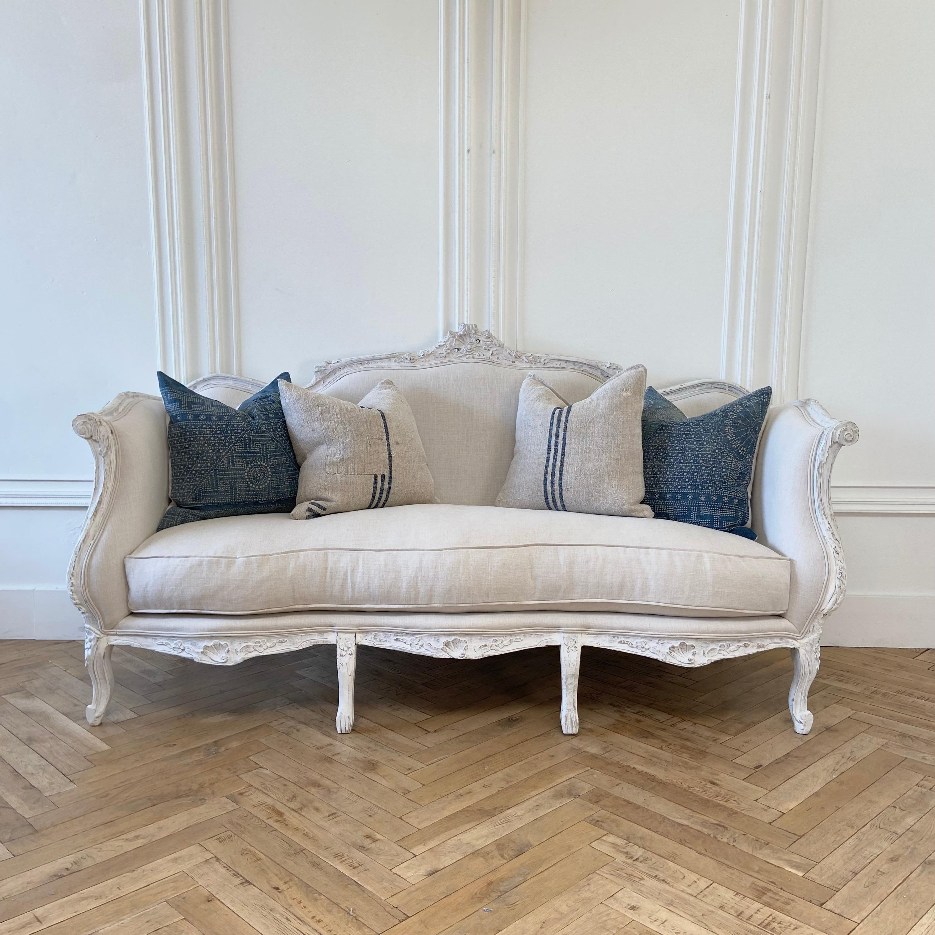 Vintage painted and upholstered Louis XV style settee painted in a soft white finish with subtle distressed edges. Upholstered in 100% Belgian Linen with flat welt piping. 
84” W x 31” D x 45” H
Seat height: 21”. 
Seat depth: 21”. 
Arm height: