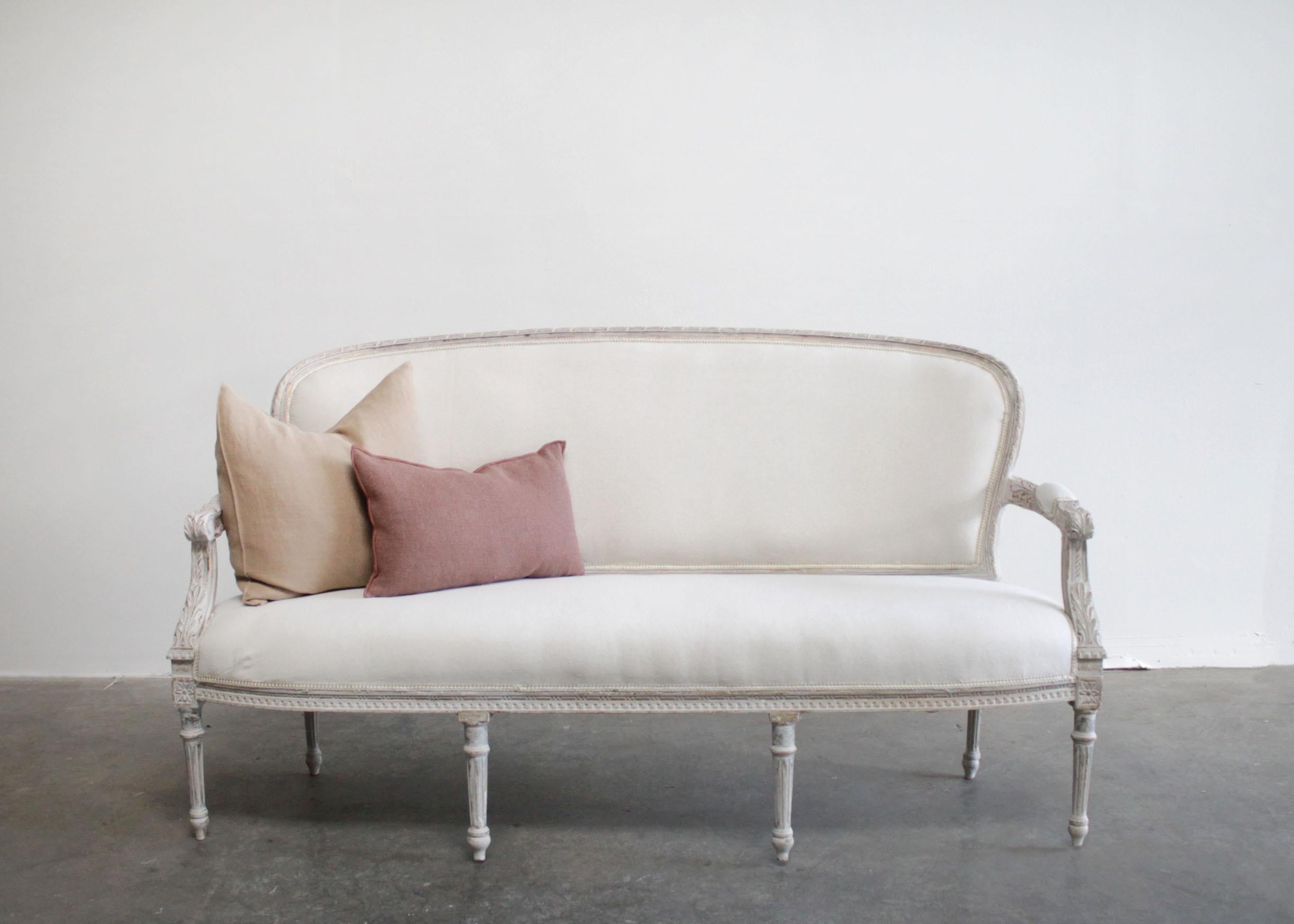 Vintage painted and upholstered Louis XVI style open arm sofa settee
Painted in a French white with subtle distressed edges, and wood showing through.
Classic fluted legs, with a medallion carving, and a curl ribbon carving.
Upholstered in a