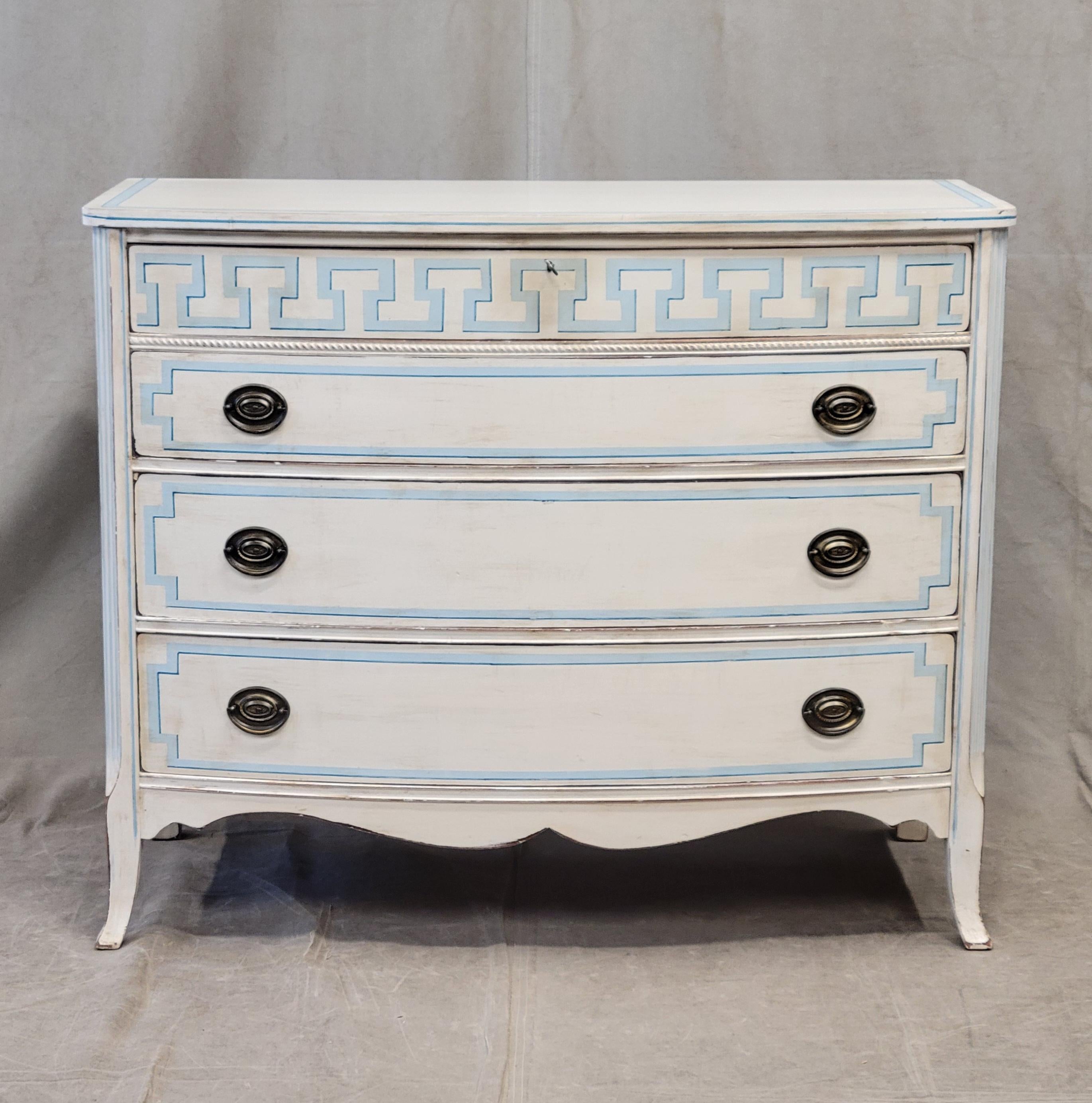 An absolutely charming vintage hand painted dresser with distressed white paint and blue trompe l'oeil French line motif. The top drawer is embellished with a stunning trompe l'oeil Greek key motif. The four drawers glide smoothly and offer plenty