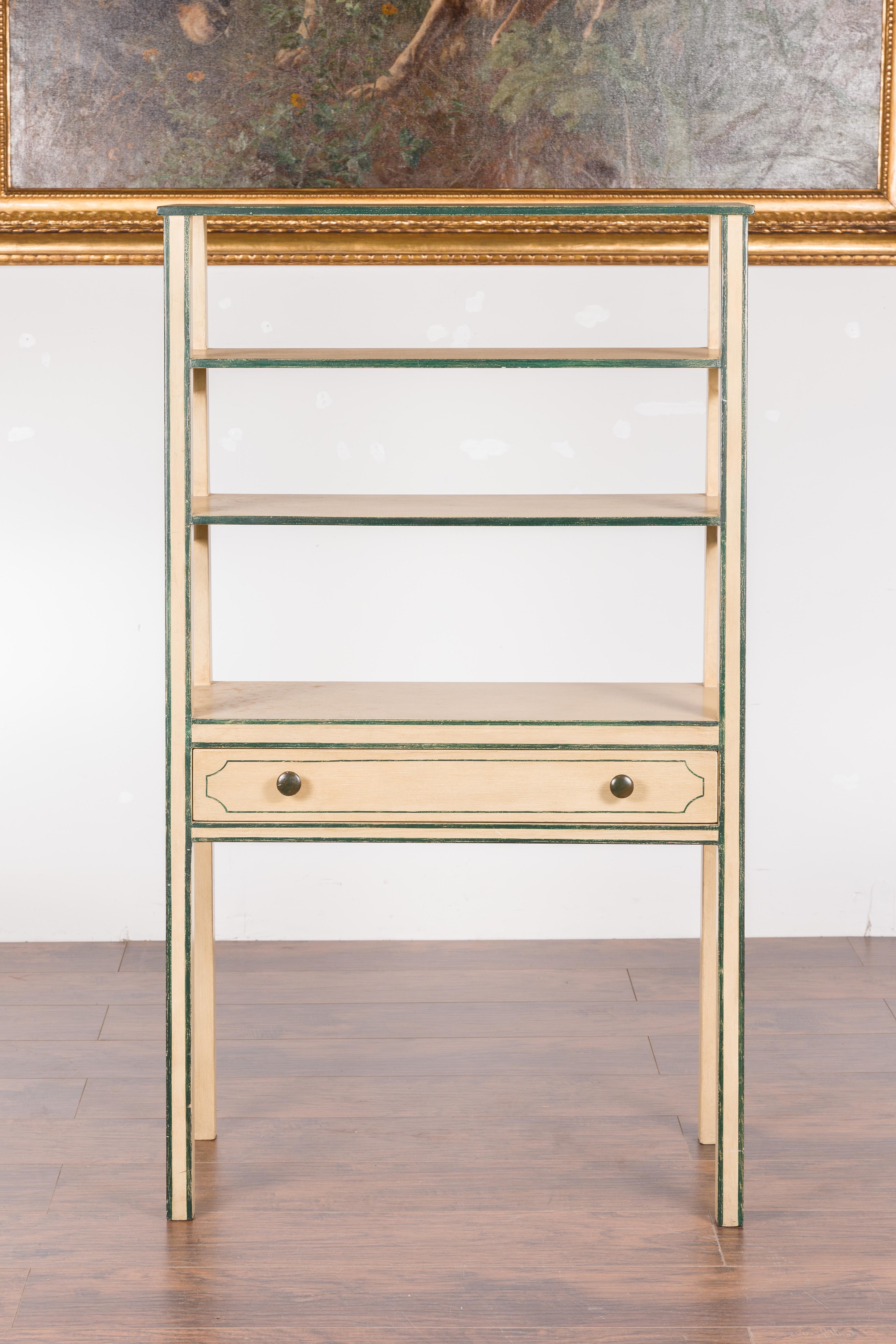 A continental vintage painted freestanding bookcase from the mid-20th century, with green accents and single drawer. Created during the midcentury period, this painted bookcase features a slanted front showcasing three open shelves sitting above a