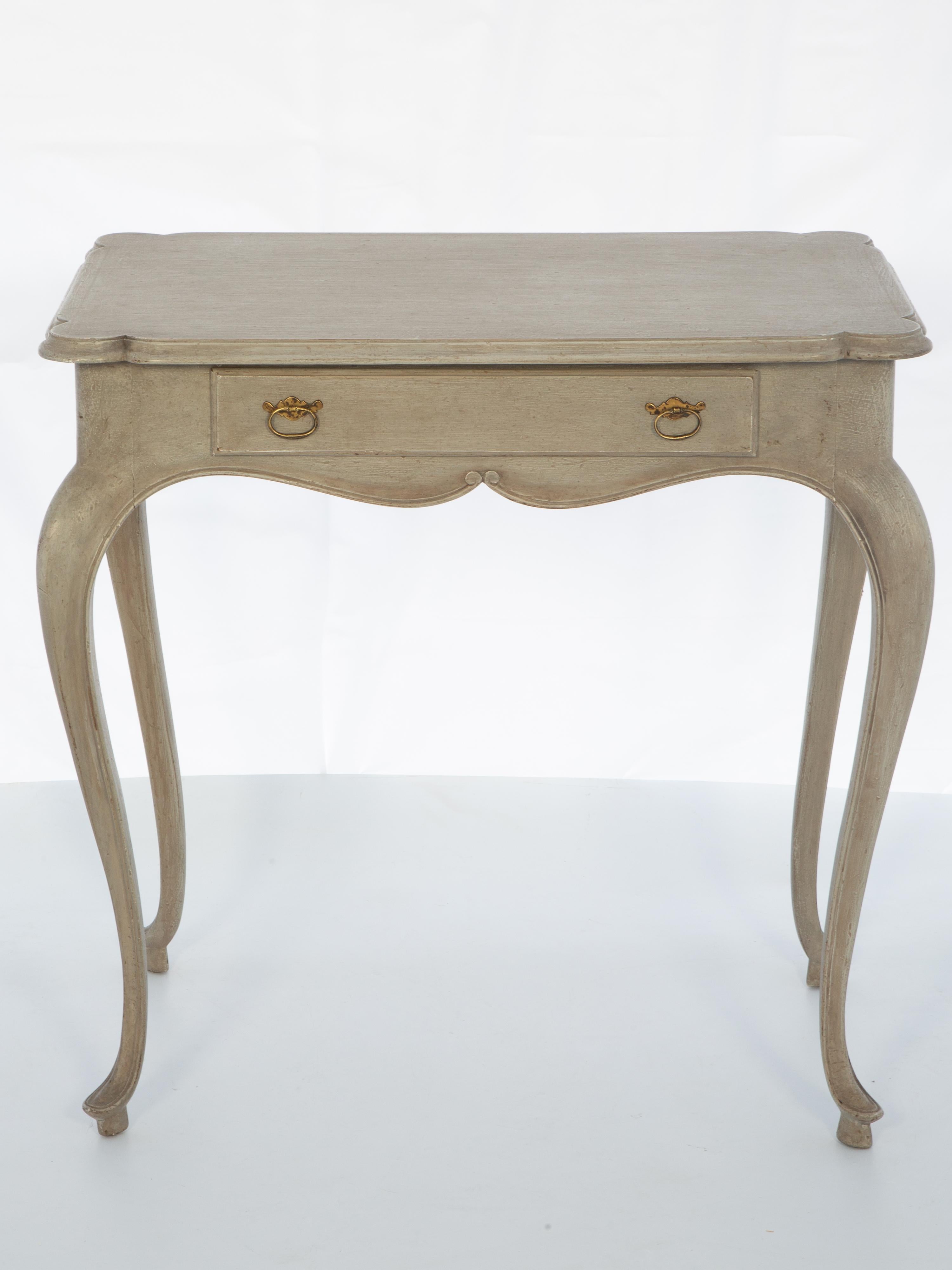 Tea table, having a painted finish in gray tones, its molded rectangular top, single frieze drawer centered with patinaed brass pulls, its serpentine apron raised on exaggerated cabriole legs, ending in hoofed feet. 

Please contact us for