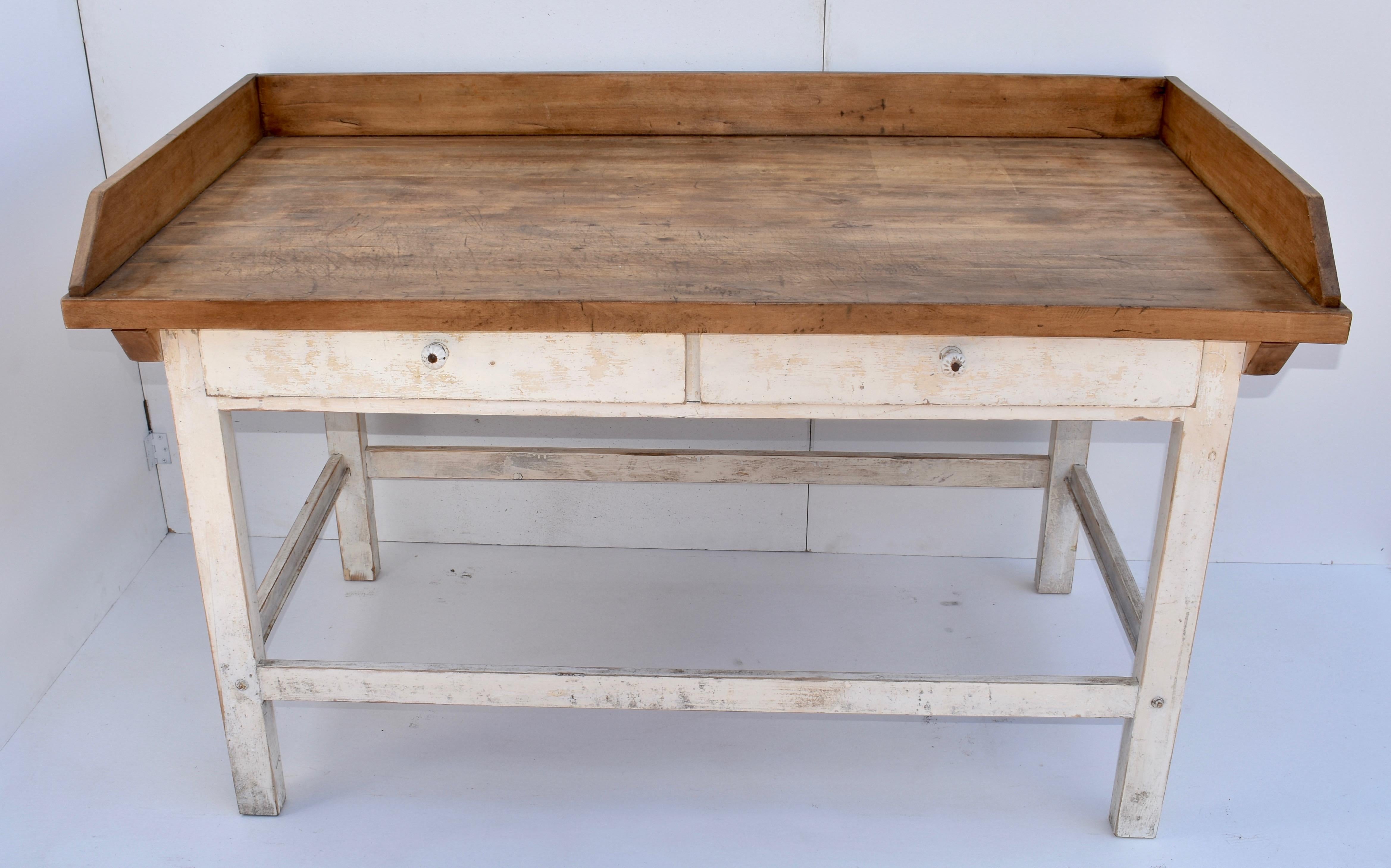 This sturdy work table has an oak top 1.5” thick with a 4” high gallery on three sides. It is pegged to a square-legged pine base through thick cleats attached to the underside. The base has well-worn stretchers all round and is finished in old worn