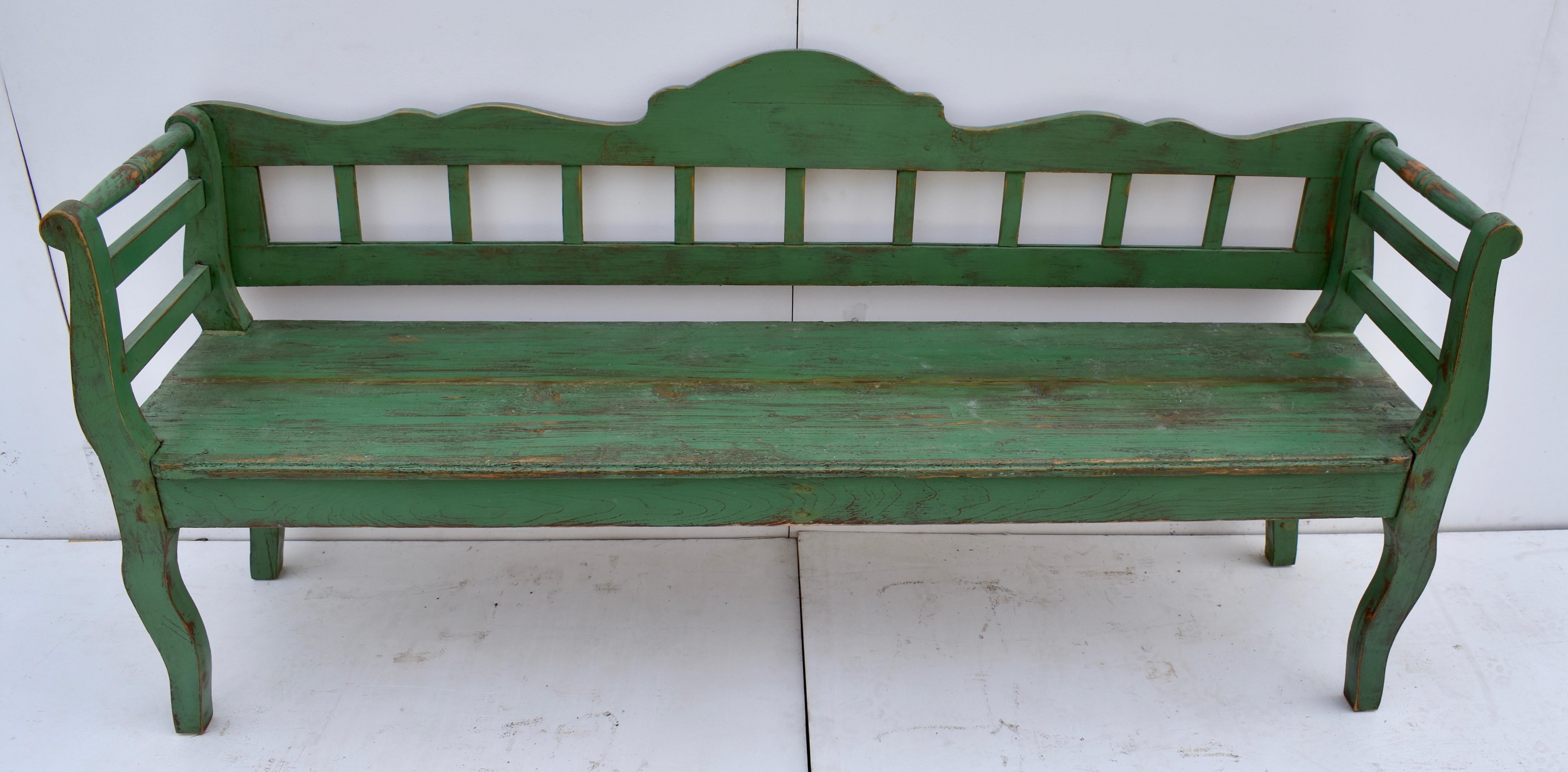 This painted Central European bench or settle, though fairly plain, has a lovely form. The scalloped top rail and plain bottom rail enclose nine simple slats, while the curvilinear legs and integral scrolled arms enclose two plain rails with a