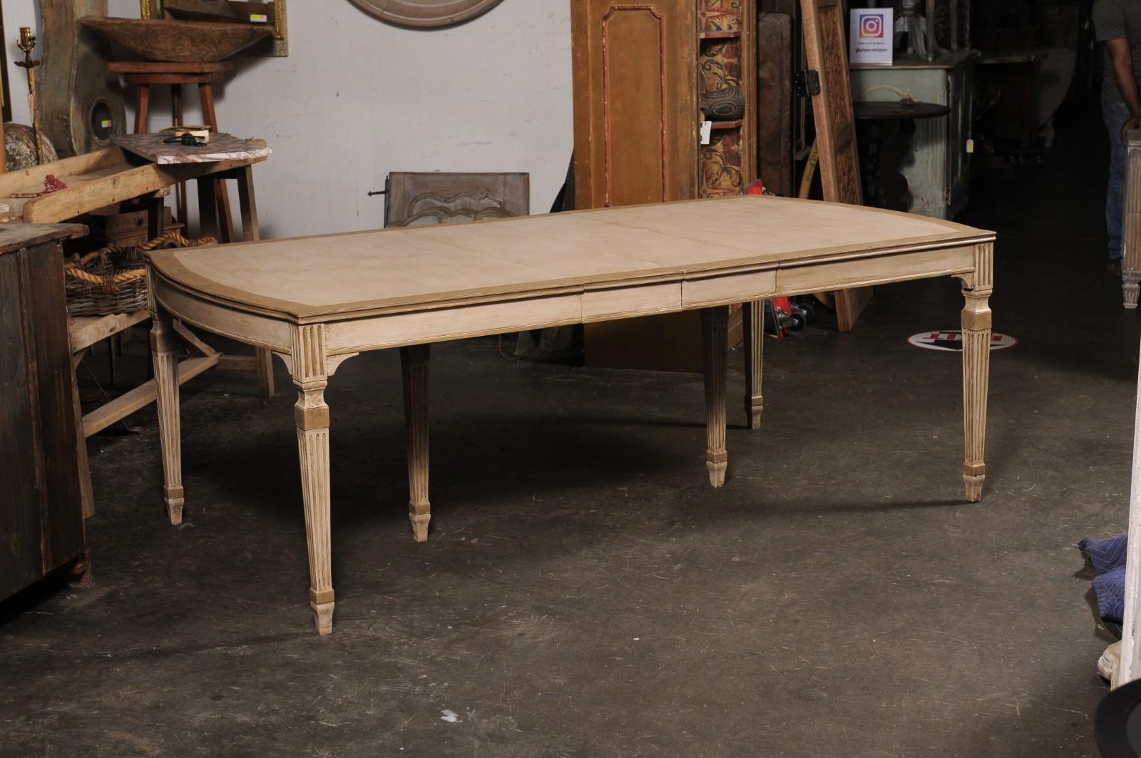 Une salle à manger vintage en bois peint américain avec des feuilles. Cette table en bois a un plateau de forme rectangulaire qui présente un subtil effet de voûte aux deux extrémités. Le tablier est conçu de manière épurée avec des moulures