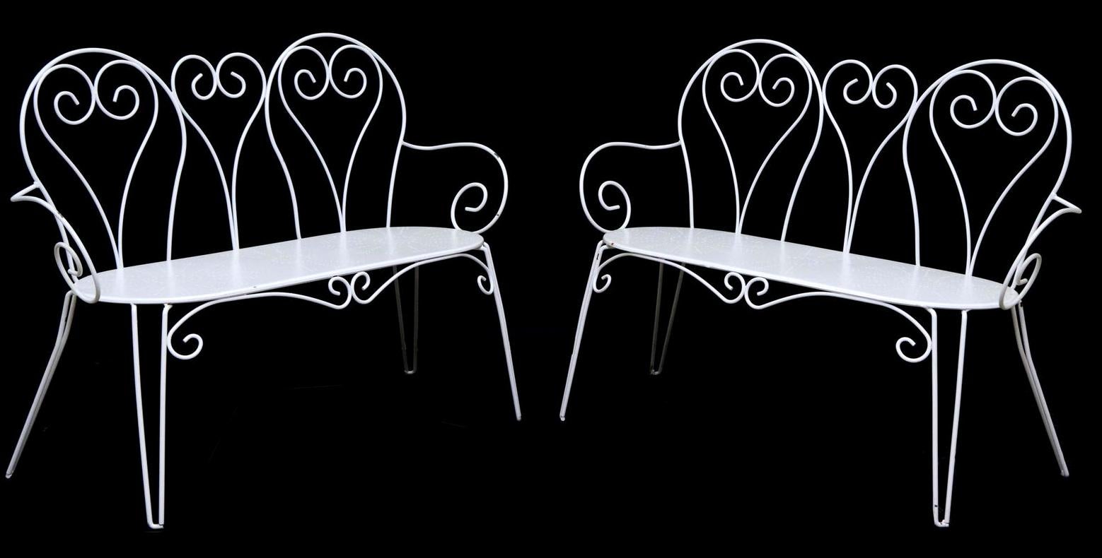 Pareja de bancos de jardín franceses antiguos, de hierro pintado, de mediados del siglo XX, con respaldo y reposabrazos de hierro forjado con volutas, sobre asiento perfilado con motivos geométricos perforados, que se eleva sobre soportes tubulares