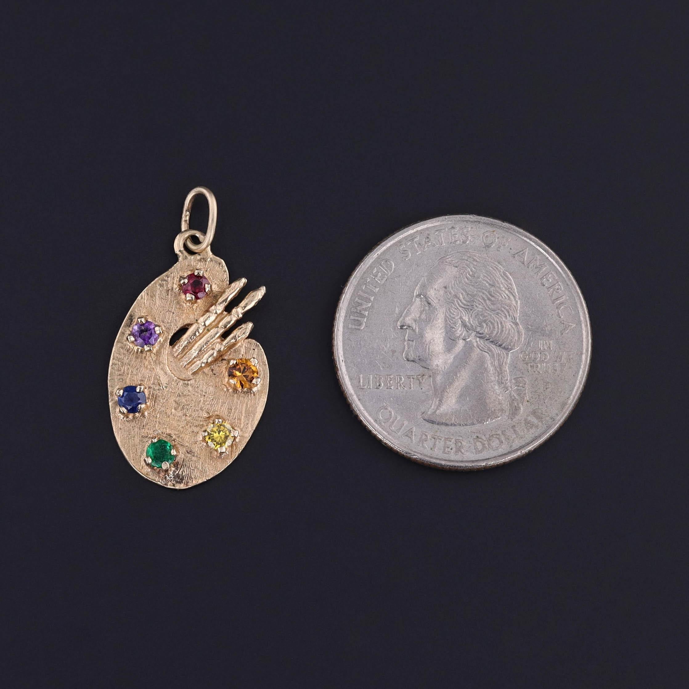 Palette de peintre vintage en or 14k avec un rubis, une améthyste, un saphir, une émeraude, un diamant jaune et une pierre de verre orange, datant des années 1960.

La pièce mesure 1,1 pouce du haut de l'anneau de saut à la base, 0,6 pouce de large