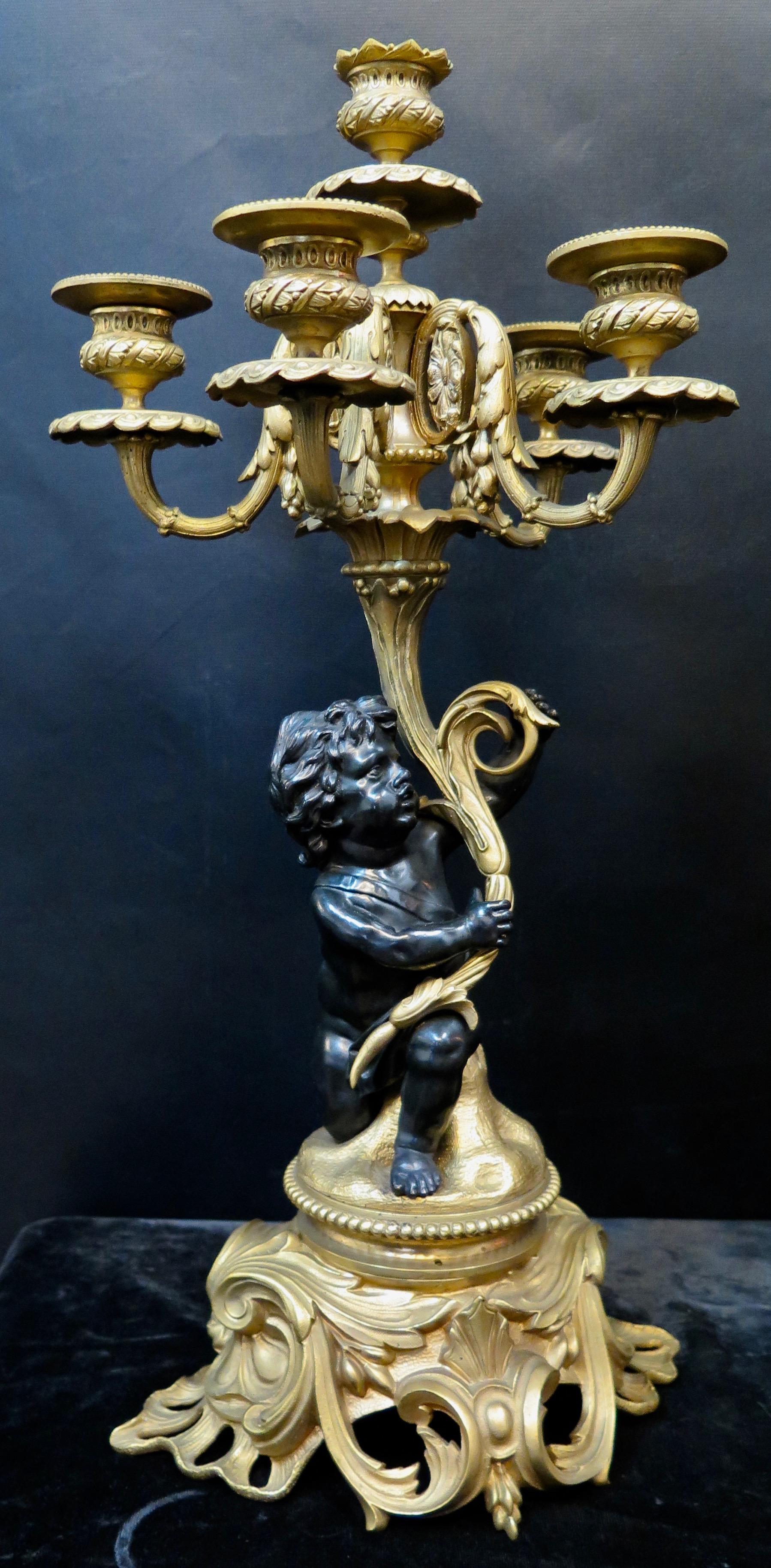 This fine antique pair of French Louis XV style gilt and patinated bronze candelabra date from the 19th century. Detailed sculpted patinated putti figures are prominently positioned holding a flowing botanical topped with five candleholders with