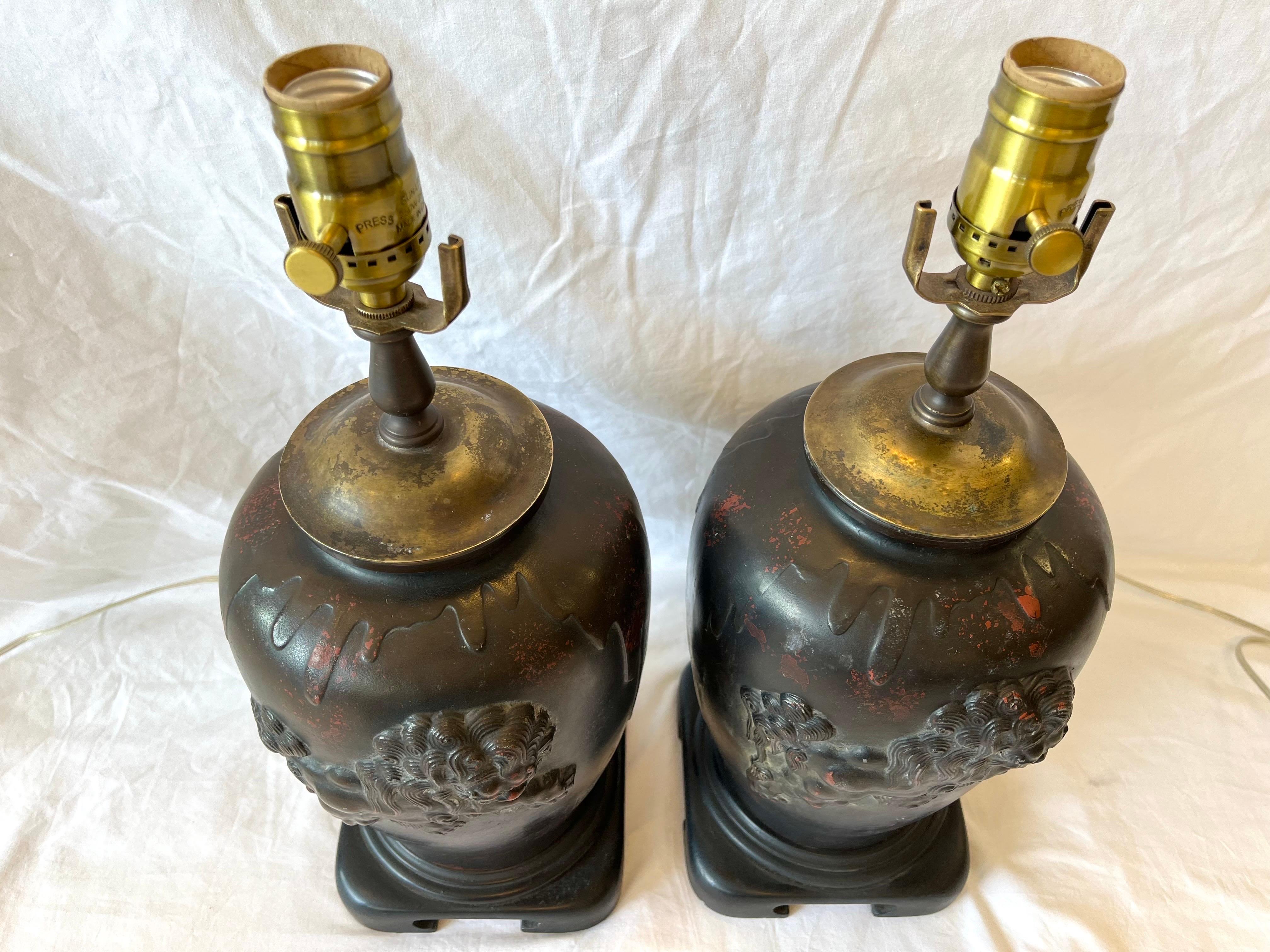 A vintage pair of signed Asian lamps with lionized Shih Tzus or Foo Dogs in a beautifully detailed high relief on the ginger jar shaped form. Each of the lamps is adorned with a leaping Foo Dog against a patinated bronze finished ground with touches