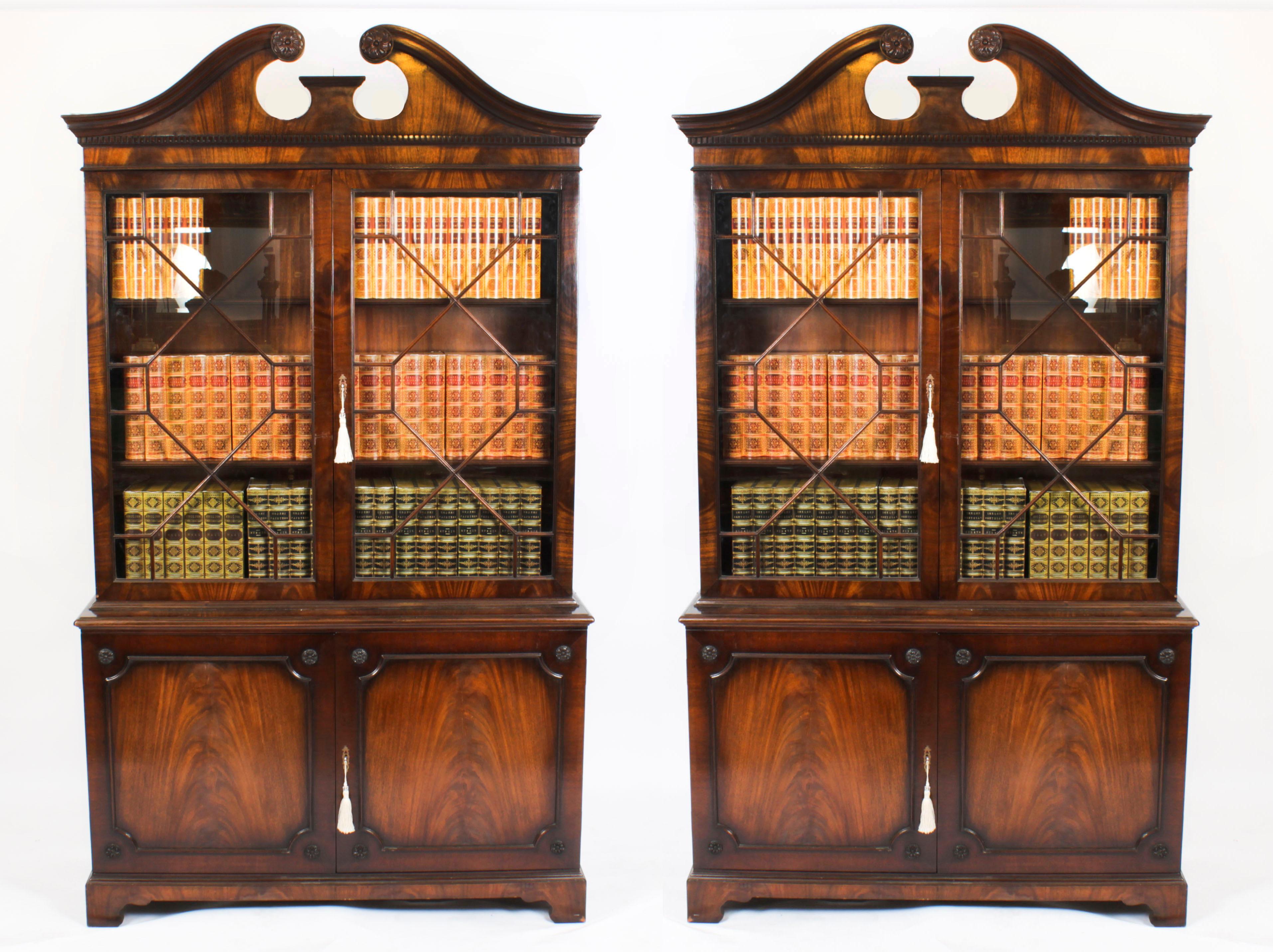 This is a superb and decorative vintage pair of Georgian revival flame mahogany bookcases, Mid 20th century in date.

The bookcases feature swan neck pediments above dentil moulding, and astragal glazed doors in the upper section revealing