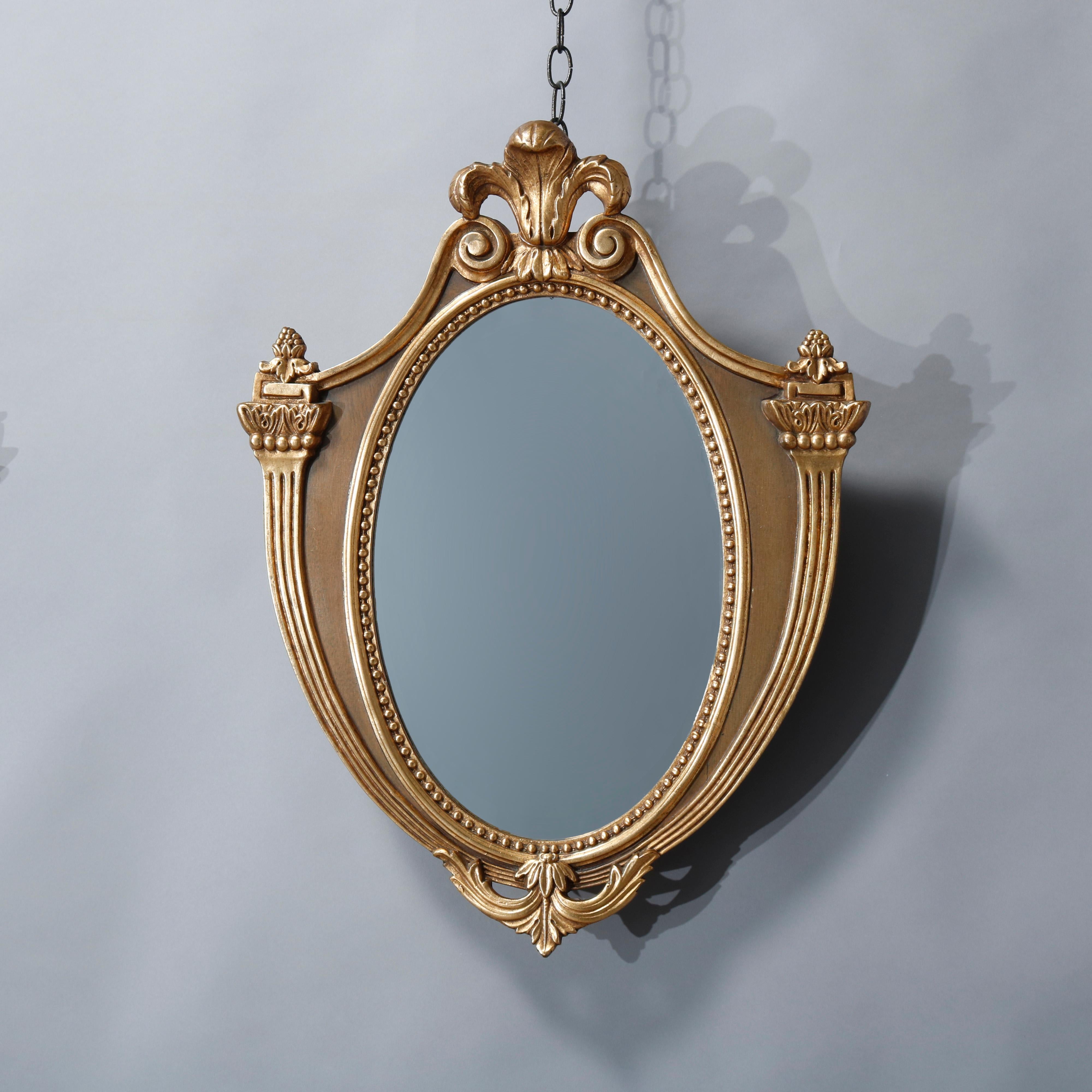 A vintage pair of French wall mirrors offer parcel-gilt mahogany frames in shield form with Fleur-de-Lis crest, beaded bordering, foliate elements and flanking stylized torchieres, circa 1940.

Measures: 26