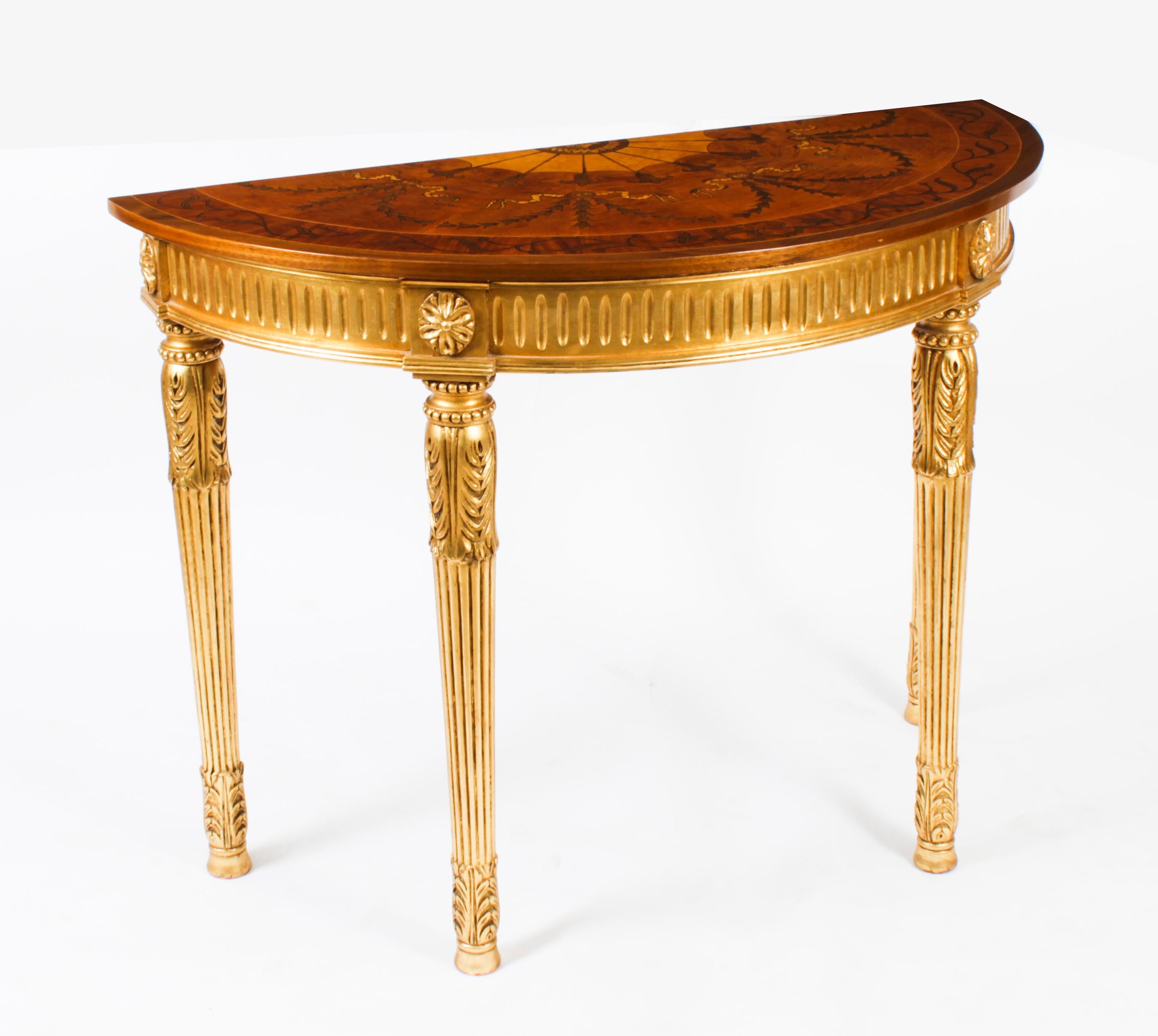 This is an exquisite pair of Sheraton Revival giltwood half moon console tables with elaborate marquetry inlaid decoration dating from the late 20th Century.
 
Sheraton is a style of English furniture that originated around 1800. This style is