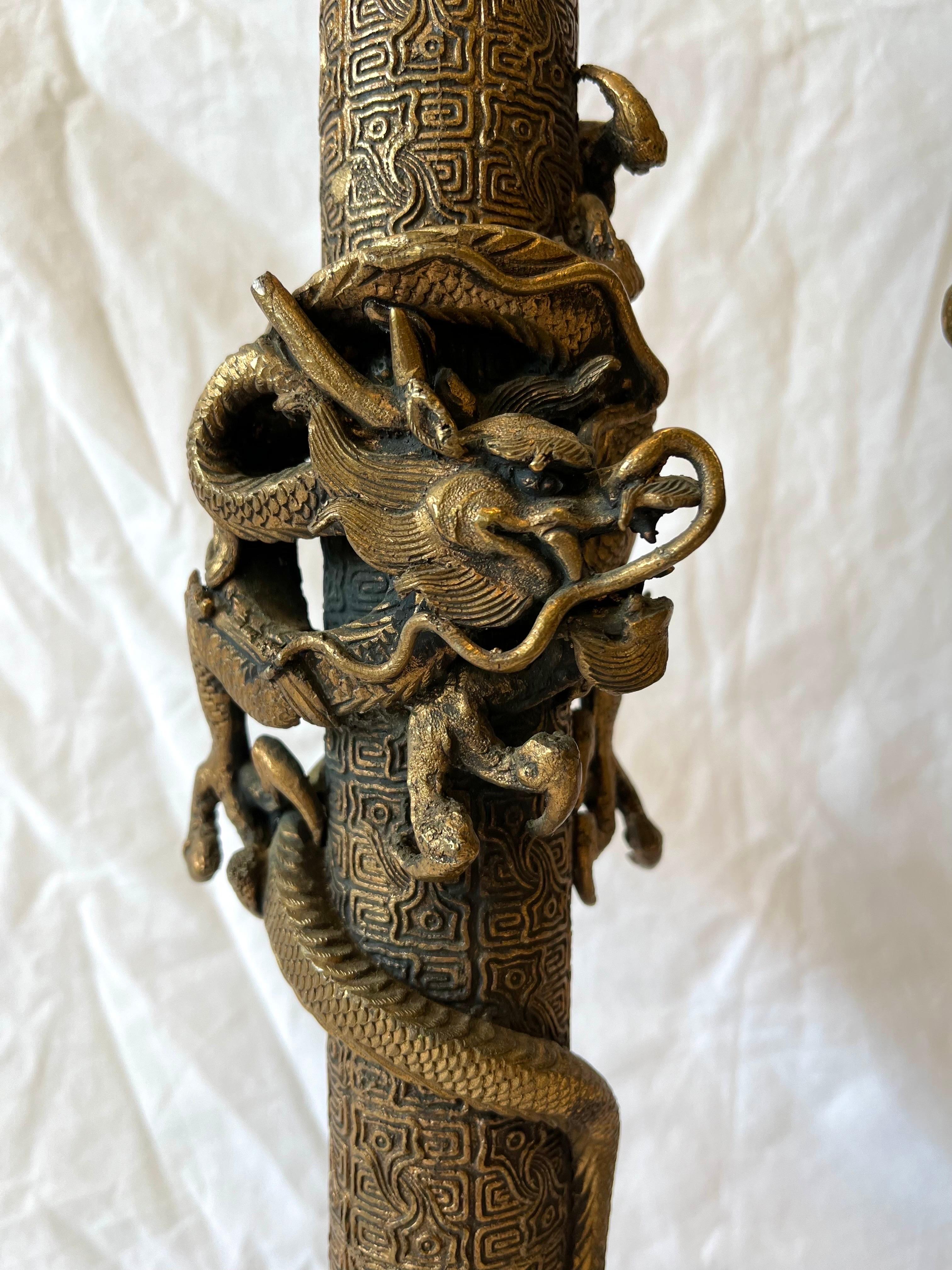 A vintage pair of coiling dragon lamps, their bodies circling a highly detailed circular column. The dragons, one facing the other on each lamp, are presented in a beautifully detailed high relief sculptural aesthetic. Each of the lamps is on a