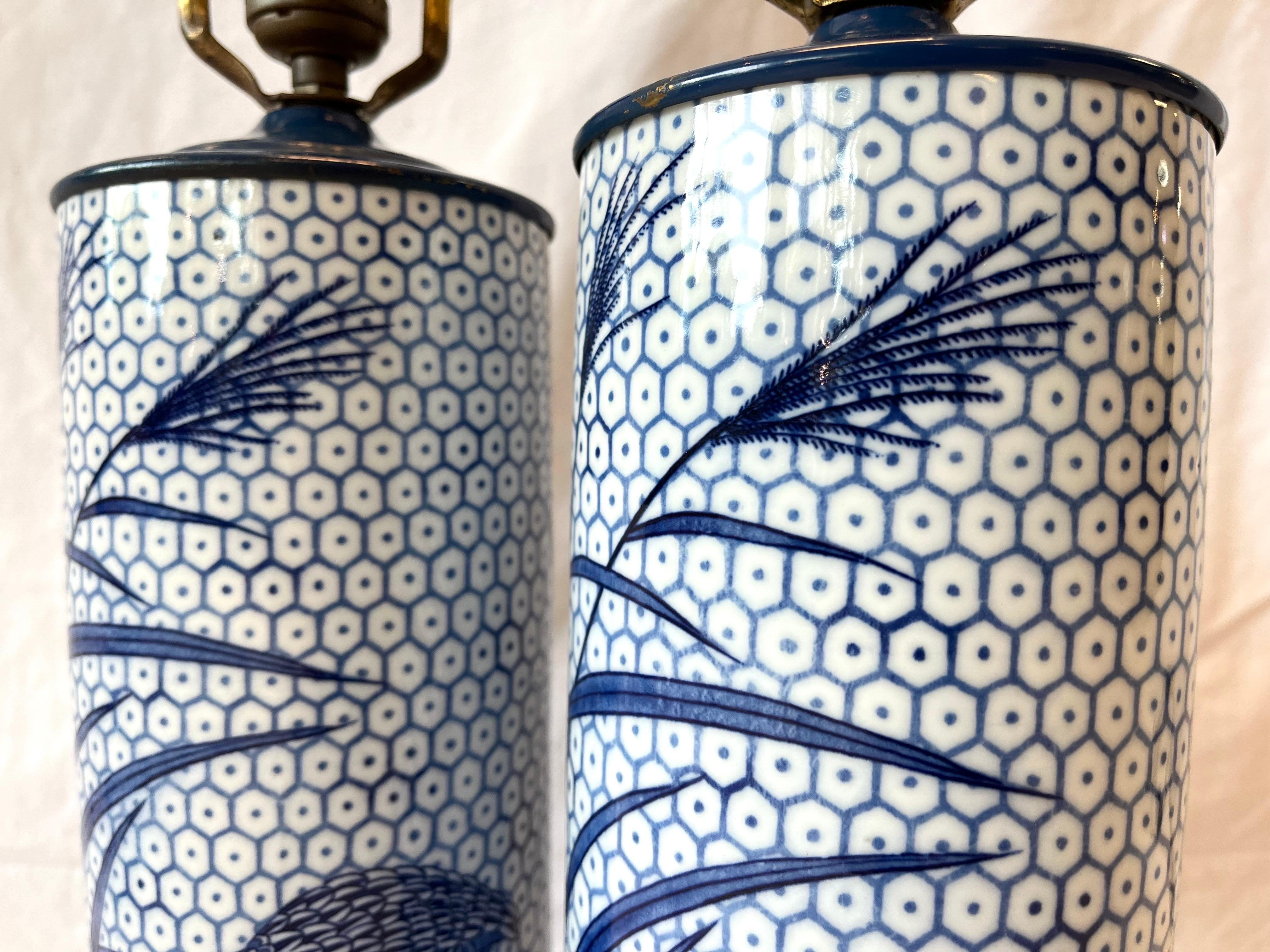 A vintage, mid 20th century era pair of blue and white cylindrical ceramic table lamps retailed by Bloomingdale's. The designer lighting department was always known as a selective and curated source for interesting and quality light fixtures.