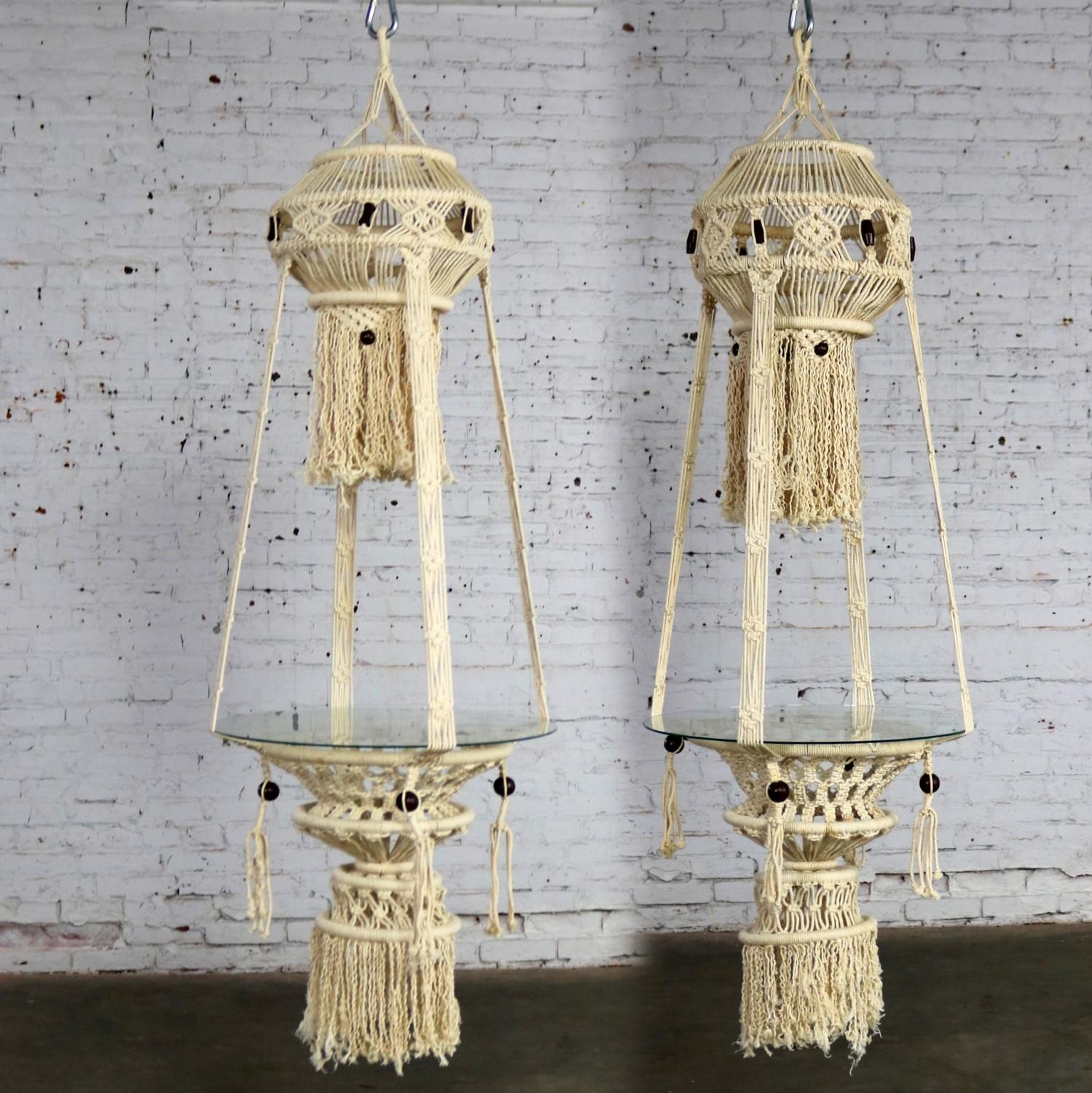 Beautiful pair of white cord macramé hanging tables with round glass tops. They are in wonderful age appropriate condition but not without minor flaws which do not take away from their overall look. Please examine photos, circa 1960s-1970s.

What an