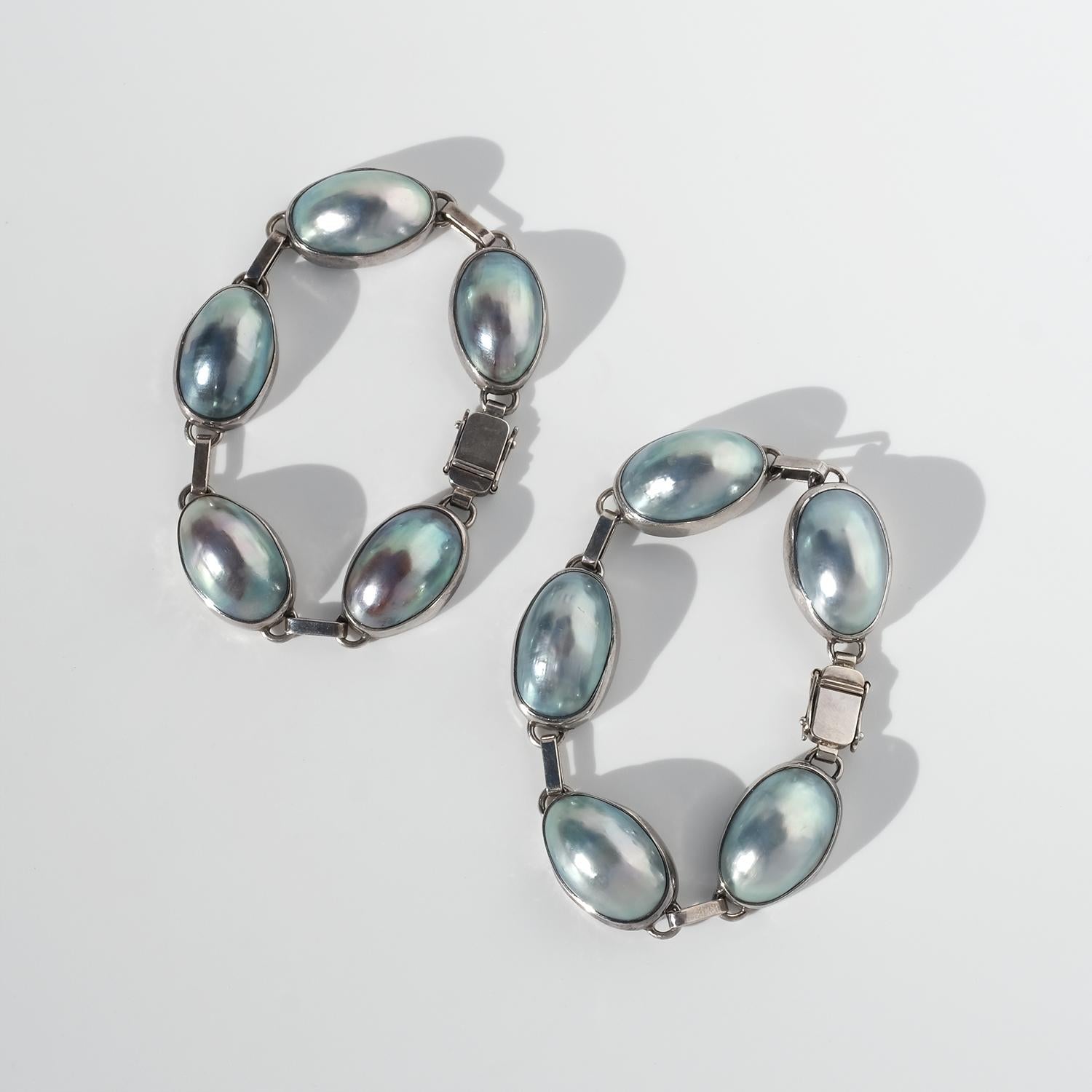 These vintage bracelets, sold as a pair, are crafted in silver and set with cabochon-shaped cultivated pearls in a cool grey tone with soft iridescence. Each pearl is held in a smooth, contoured bezel that echoes the oval form and gives the links a