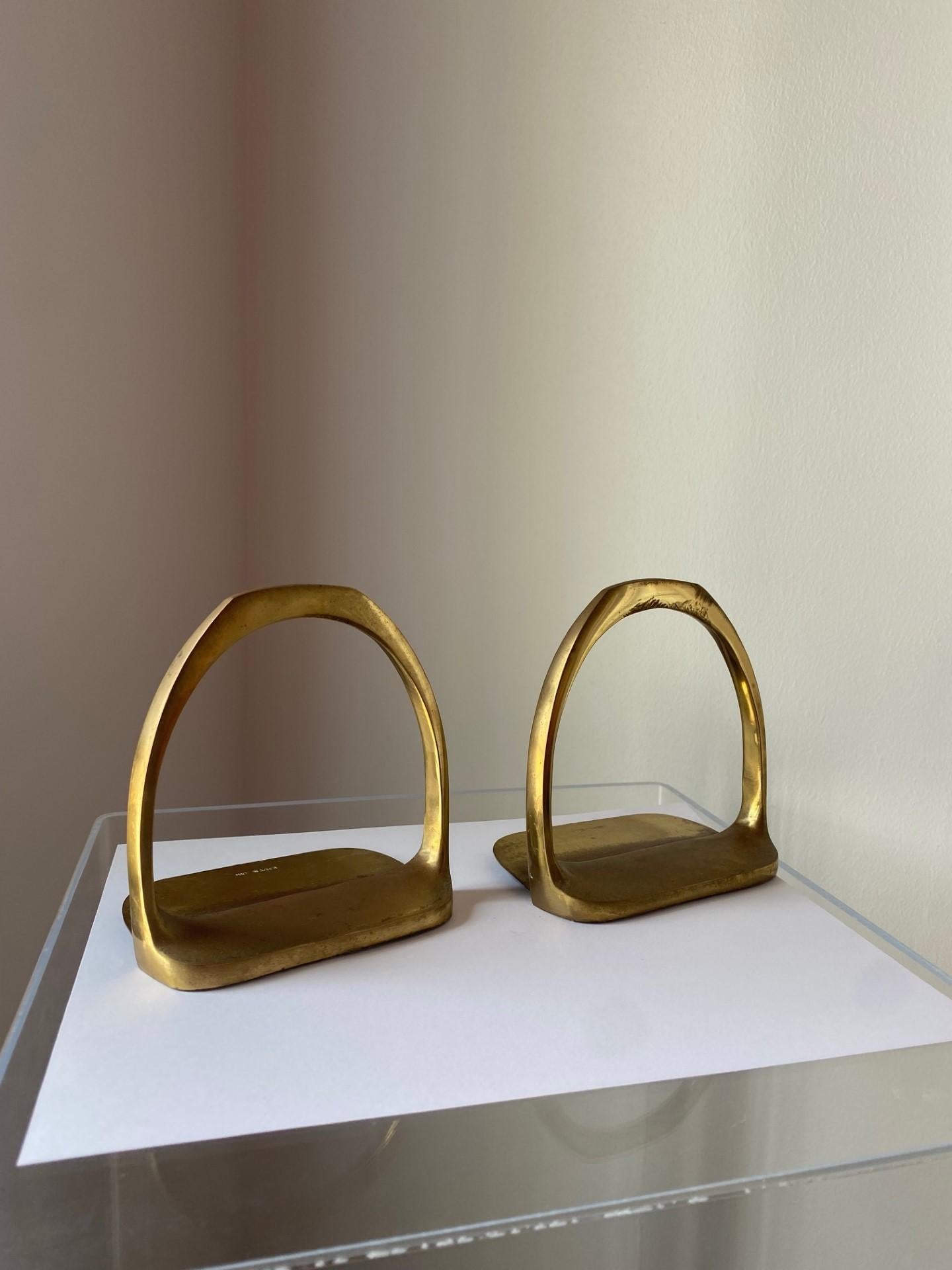 Beautiful pair of horse saddle stirrup bookends in brass.  This beautiful set is sure to create interesting impact in your décor or office.  The brass shapes are light on the eye but full of style.  The patina enhances the style and become an