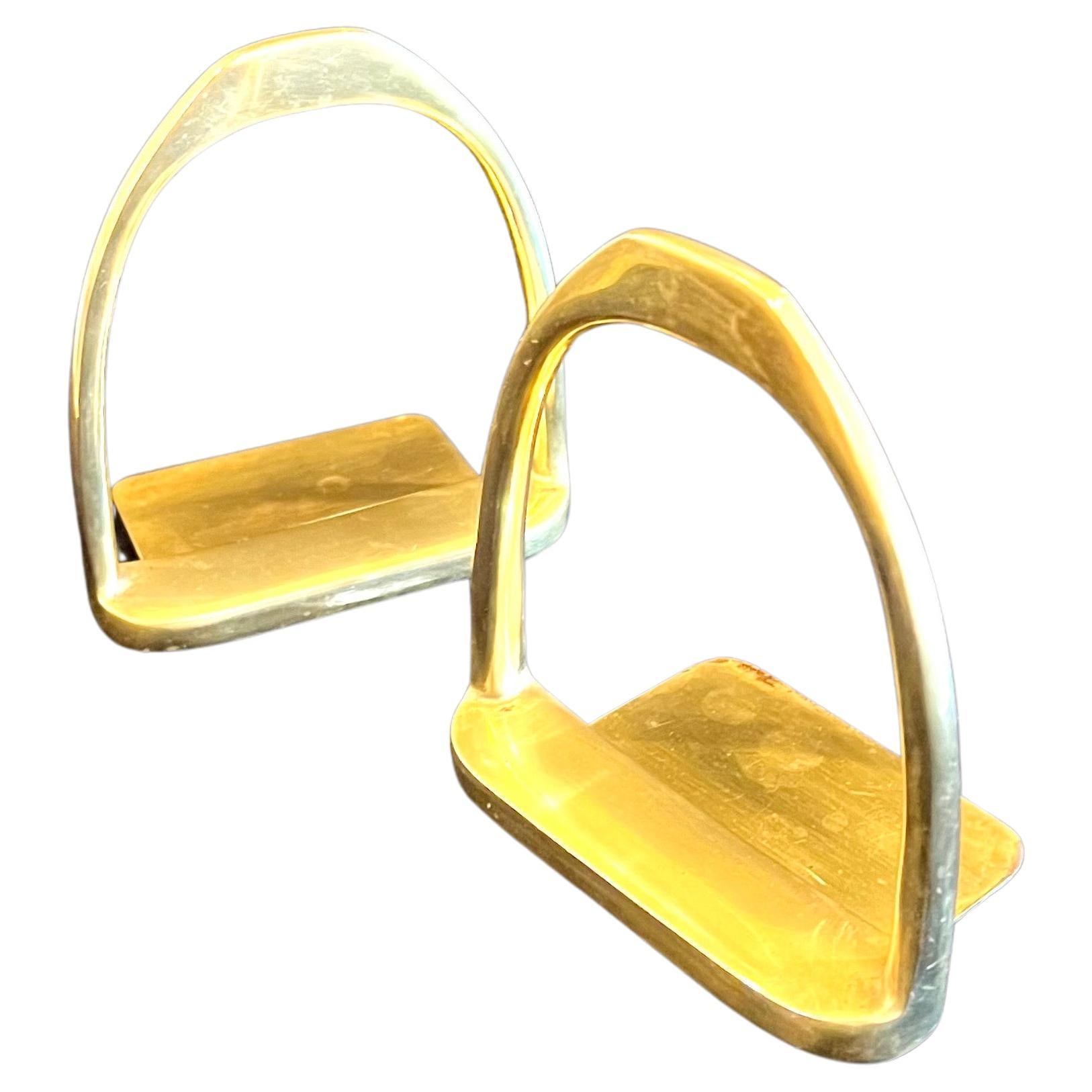 Beautiful pair of horse saddle stirrup bookends in brass.  This beautiful set is sure to create interesting impact in your décor or office.  The brass shapes are light on the eye but full of style.  The patina enhances the style and become an