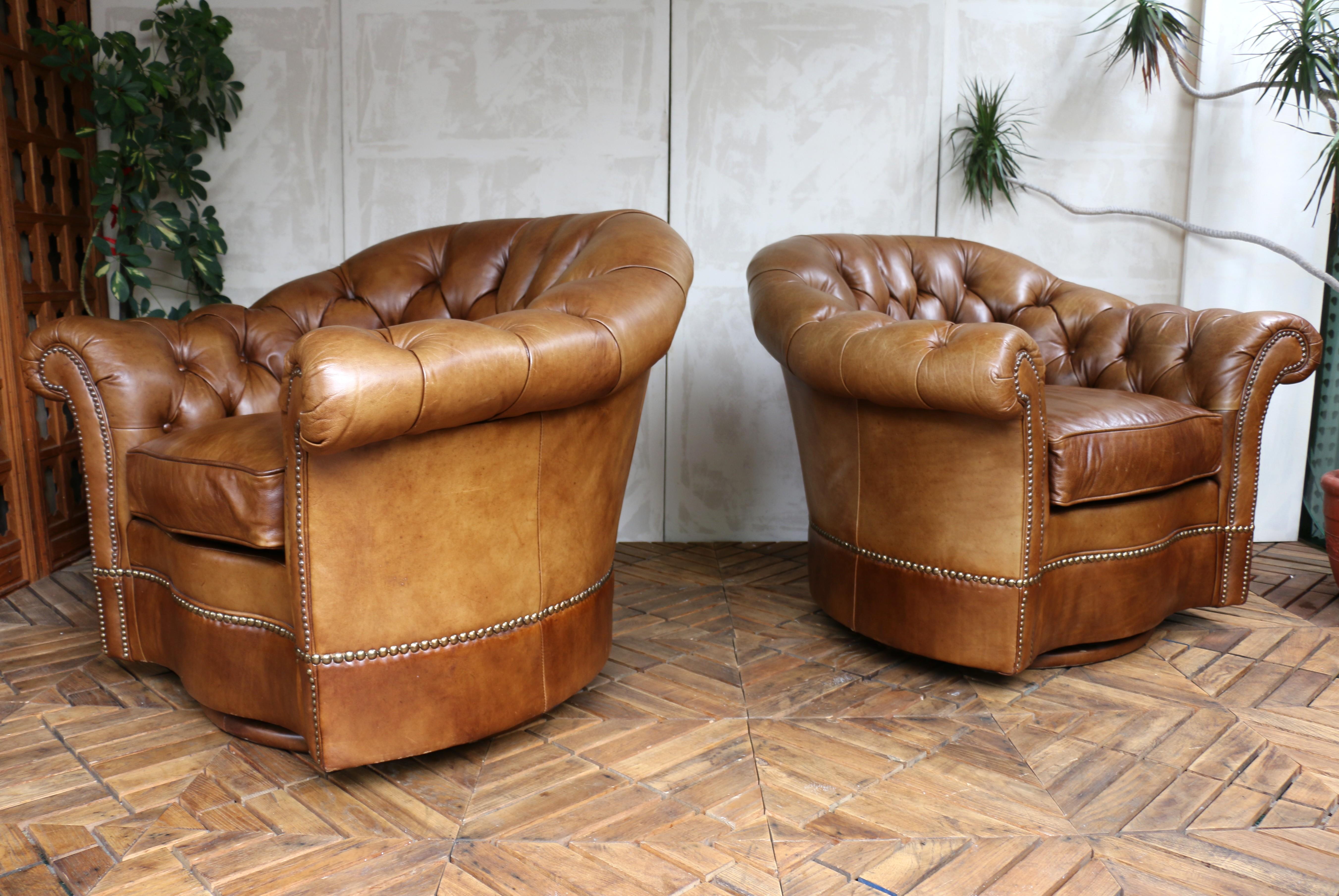 Introducing this pair of classic Chesterfield swivel club chairs manufactured by Century Furniture company, recognized for producing high-quality furniture. They are upholstered in rich brown leather, which develops a unique patina over time, adding