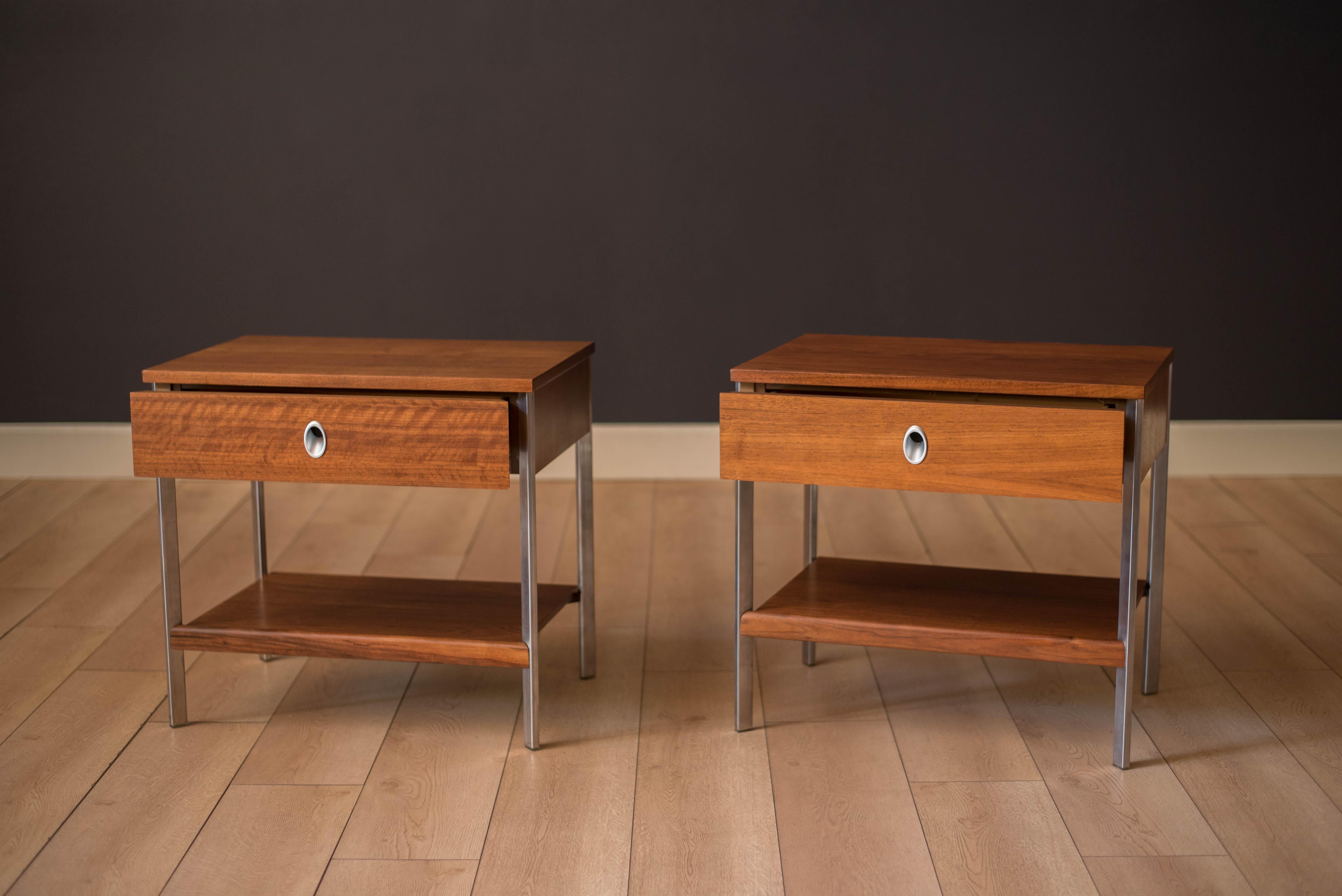 Mid-Century Modern pair of nightstands in walnut manufactured by Vista of California circa 1960's. Each bedside table includes one drawer accented with a unique polished aluminum pull. Features a lower tier display shelf for additional storage