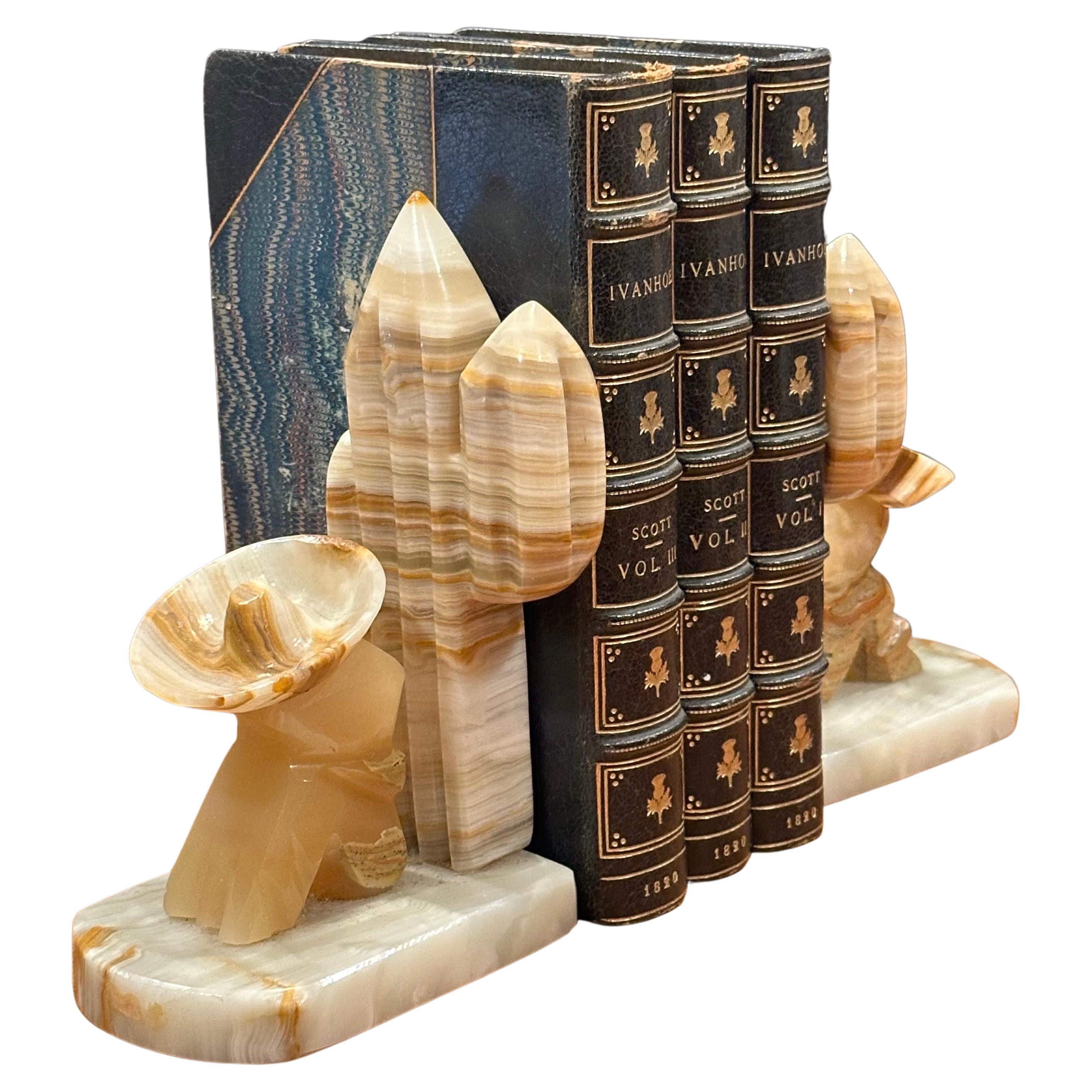 Nice vintage pair of carved Mexican onyx stone bookends, circa 1970s.  The bookends depict a sleeping man with poncho and sombrero sitting by a cactus; they have wonderful veining and translucent beauty. The pair are in very good vintage condition