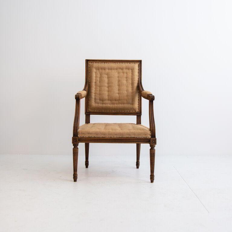 A pair of Louis XVI hand carved solid wood fauteuil armchairs from France upholstered in natural linen burlap. Armchairs have exquisite hand carved details in good patina condition. Visible nail heads secure the traditional burlap upholstery