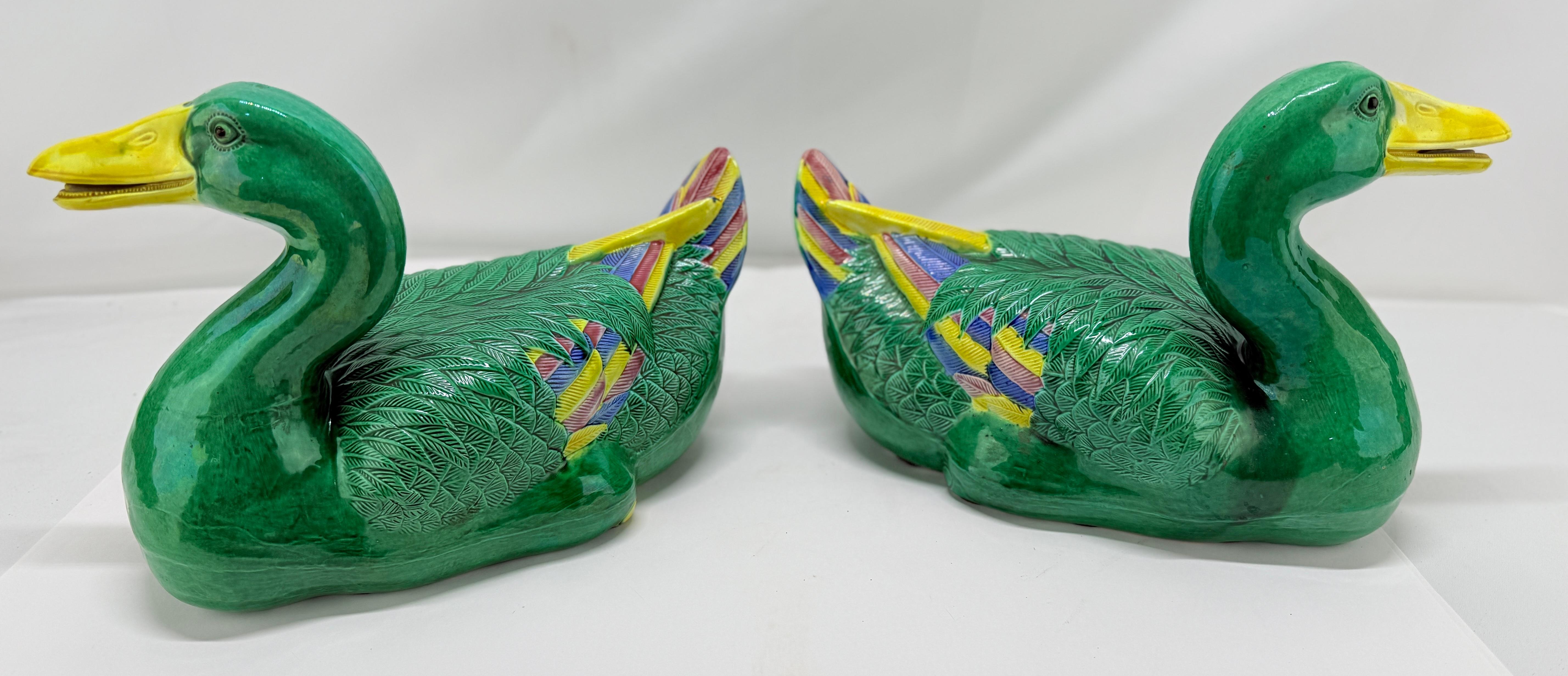 A bold and animated pair of Chinese porcelain duck-form models, likely dating to the mid-20th century, each rendered with distinctive enamel coloration and incised surface detail. Modeled as a pair of opposing drakes, the bodies are covered in a