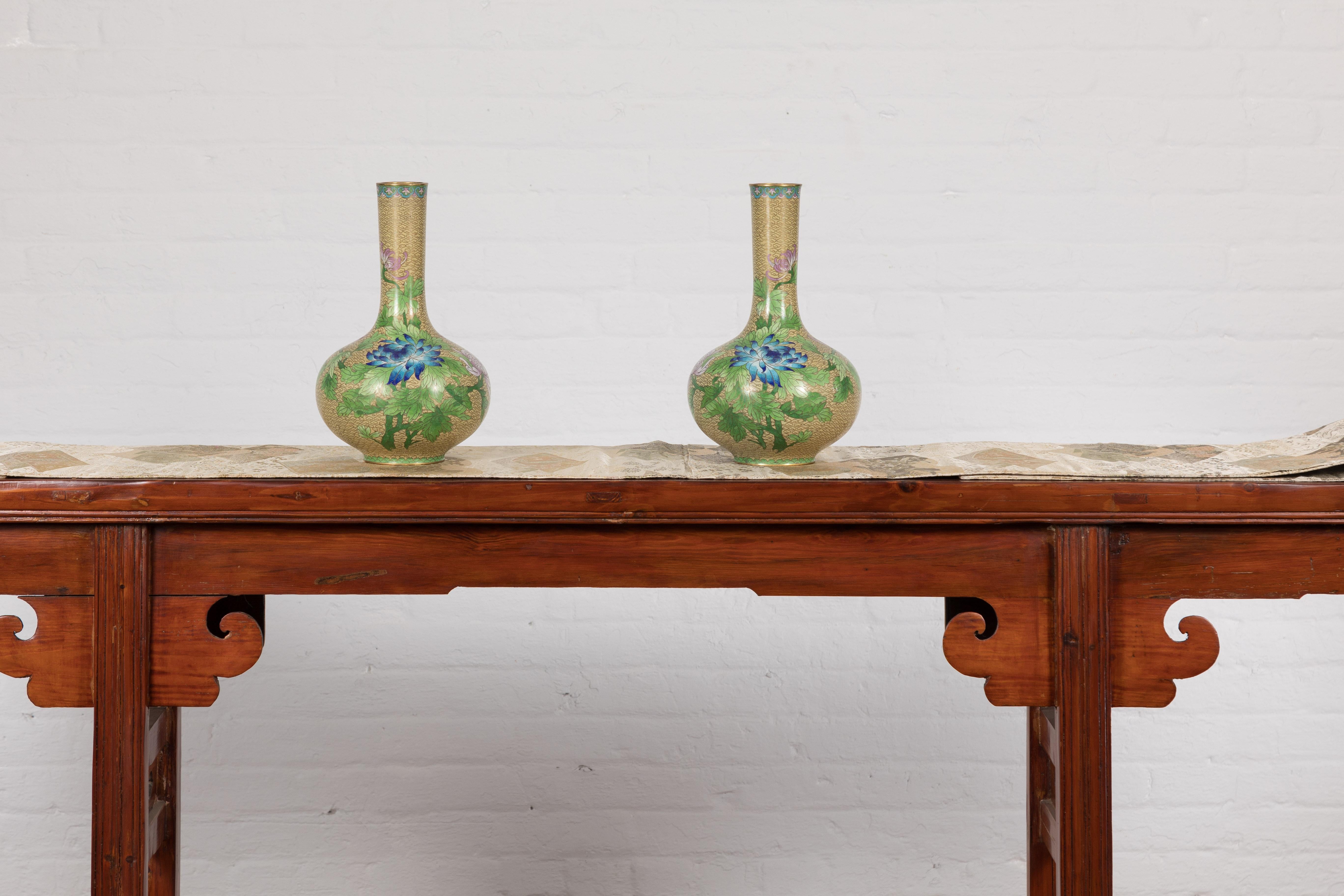 A vintage pair of Chinese vases from the mid 20th century with floral cloisonné décor. Welcome to a symphony of color and craftsmanship, presented by this vintage pair of Chinese vases that hail from the mid-20th century. A treasure for collectors