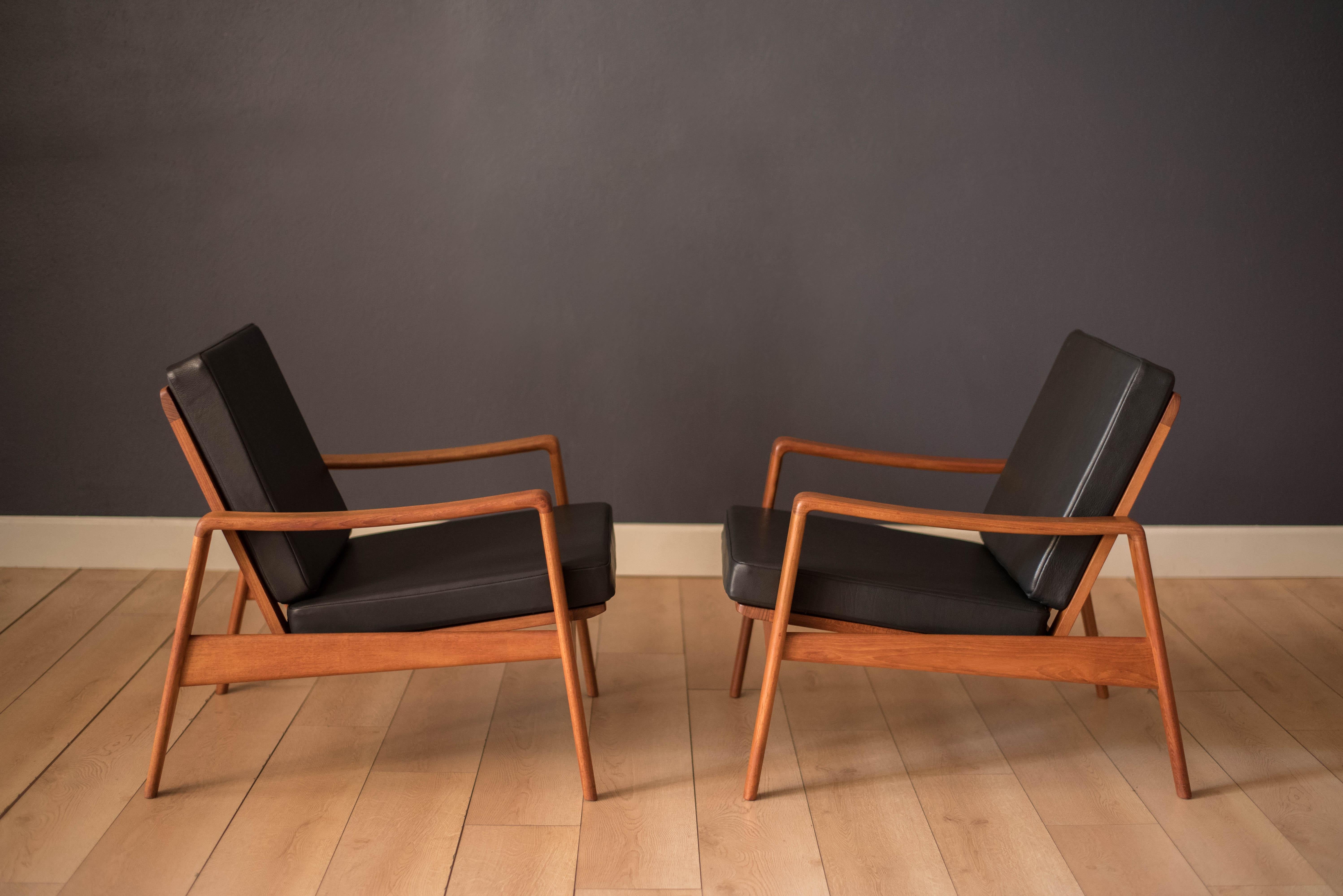 Mid-Century Modern pair of easy lounge chairs in teak designed by Arne Wahl Iversen for Komfort, Denmark. This set includes brand new foam seats and black leather. Sculptural modern teak frames can be displayed at any angle with a unique tapered