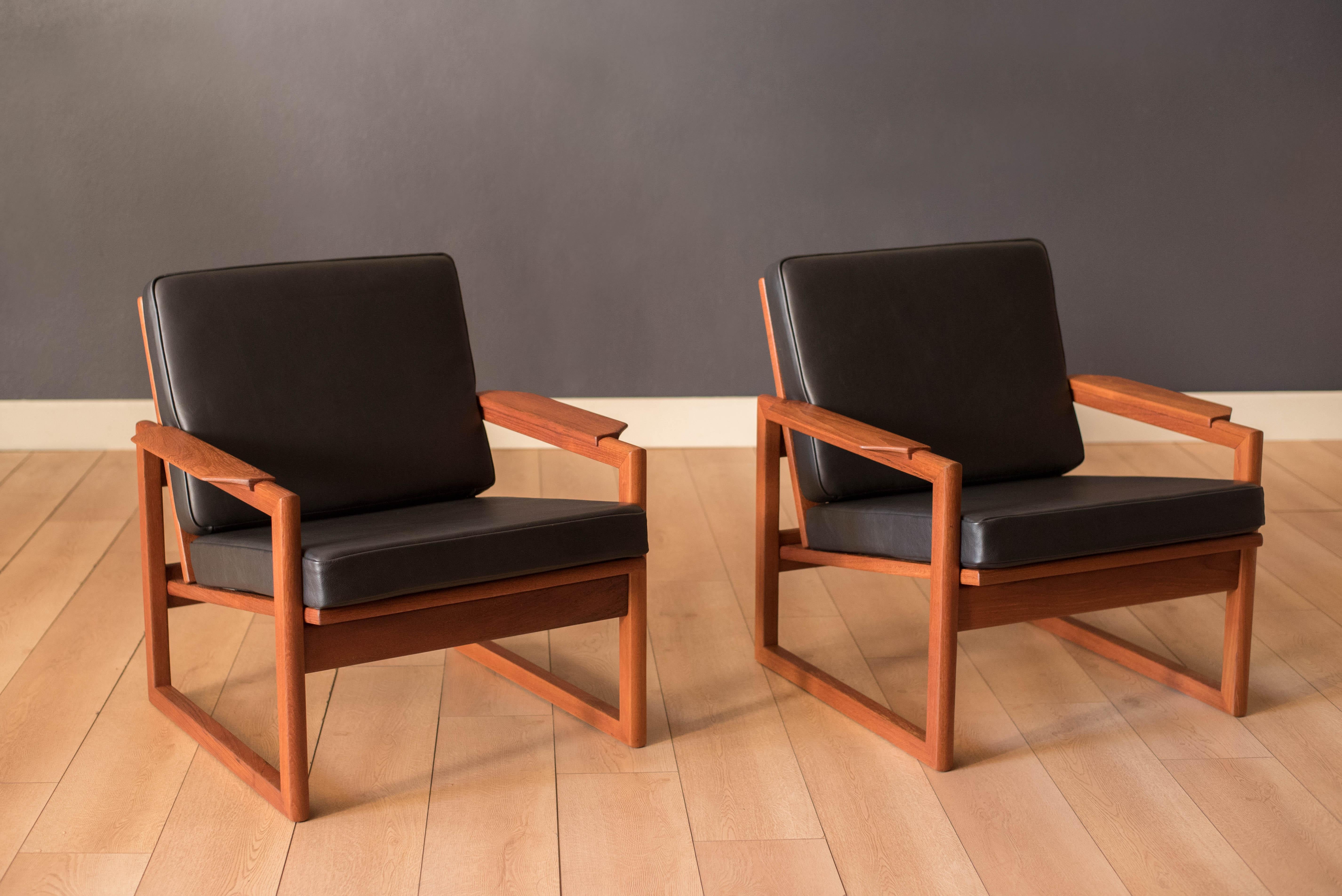 Mid Century Modern pair of lounge chairs in teak designed by Sven Ellekjaer, imported by Selig, Denmark. This set includes brand new wide foam seats in matte black leather. Features sculptural armrests with a slatted backrest support that can be
